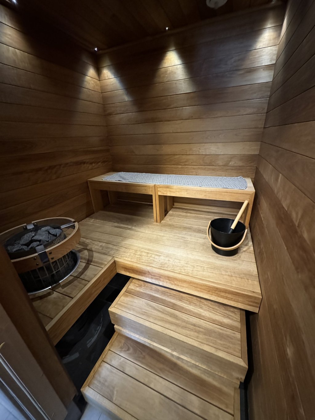 Modern wood sauna interior with tiered benches, electric heater, and bucket accessory