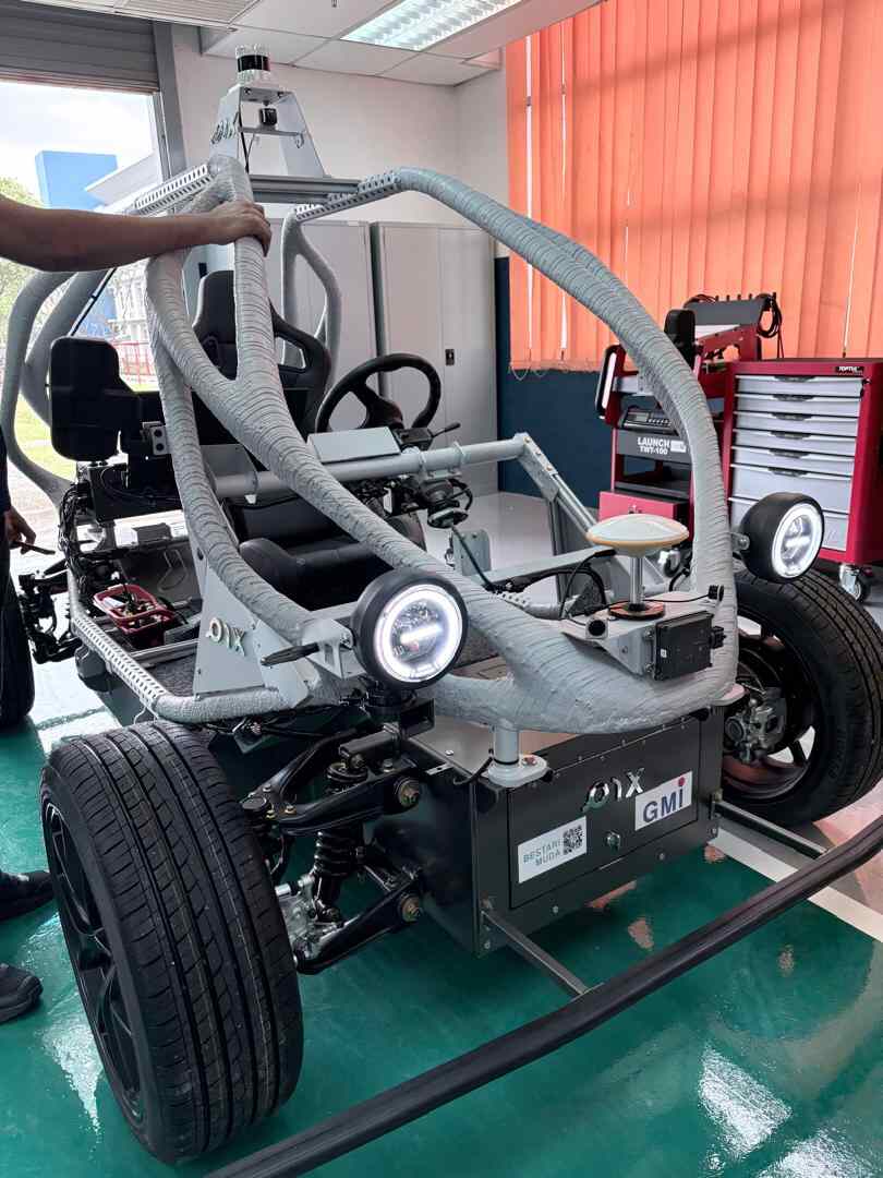 Custom-built autonomous electric vehicle prototype with sensors and roll cage in a workshop environment.