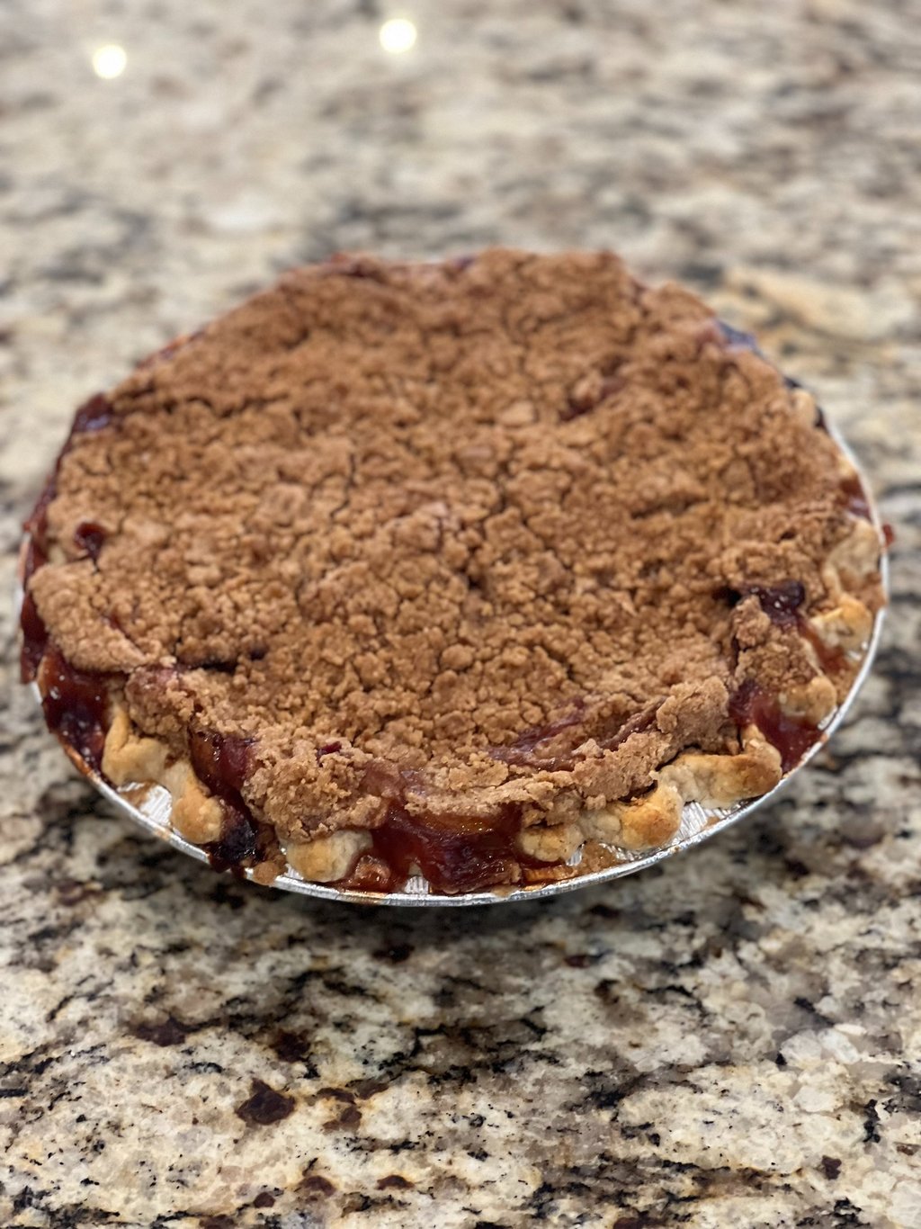 Freshly baked peach crumble pie with a golden streusel topping on a granite countertop.