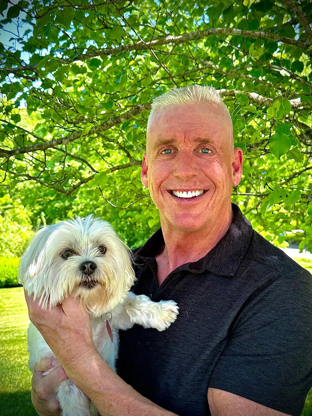 a man in a black shirt is holding a white dog; Tom O'Brien, Owner, Tymeless Properties