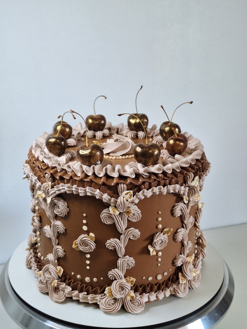 Elegant chocolate vintage cake with ornate piping and gold-dusted cherries on top.