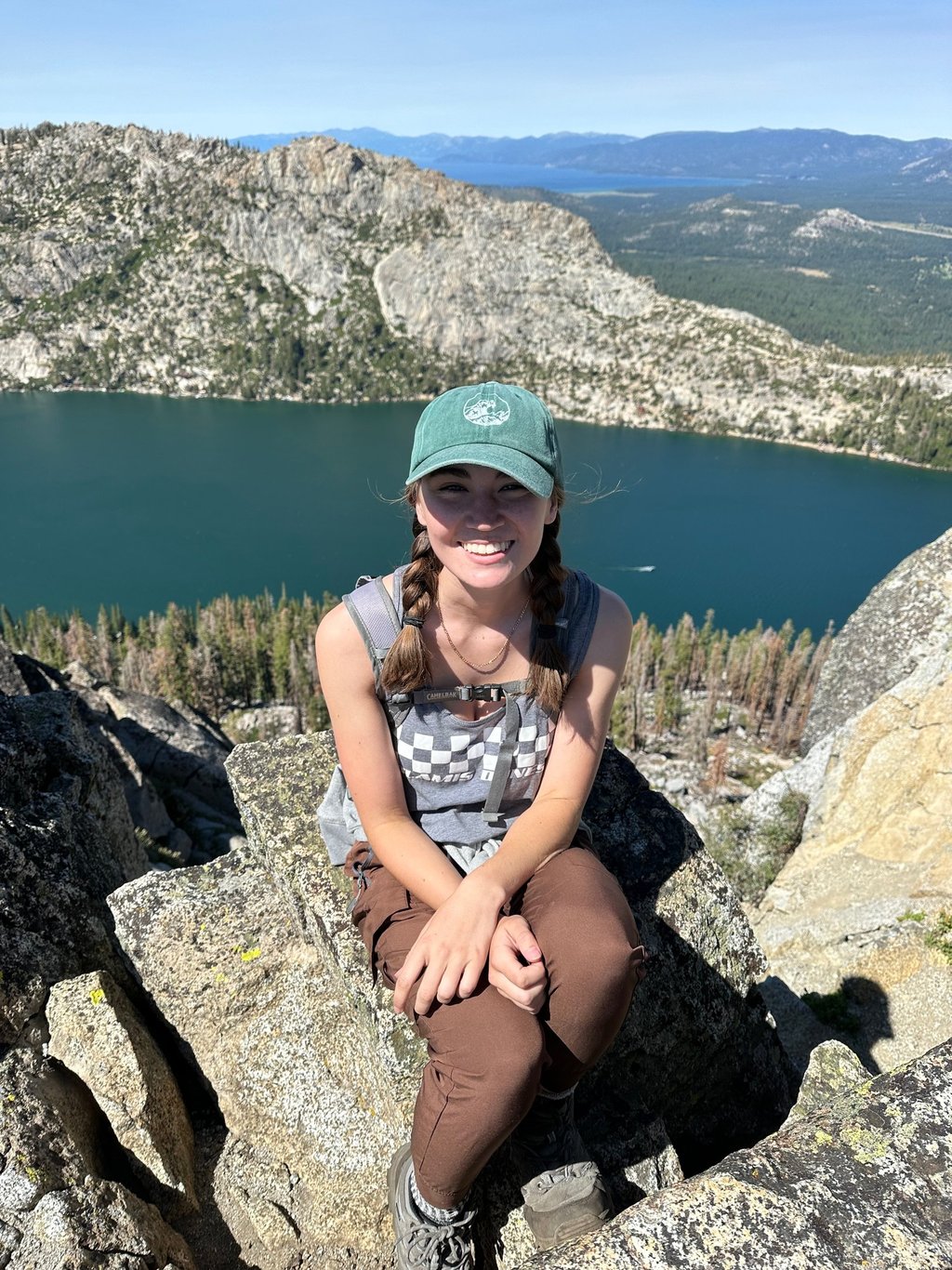 the author sitting on a rock in the mountains. in the background is a lake and a forest of pine.