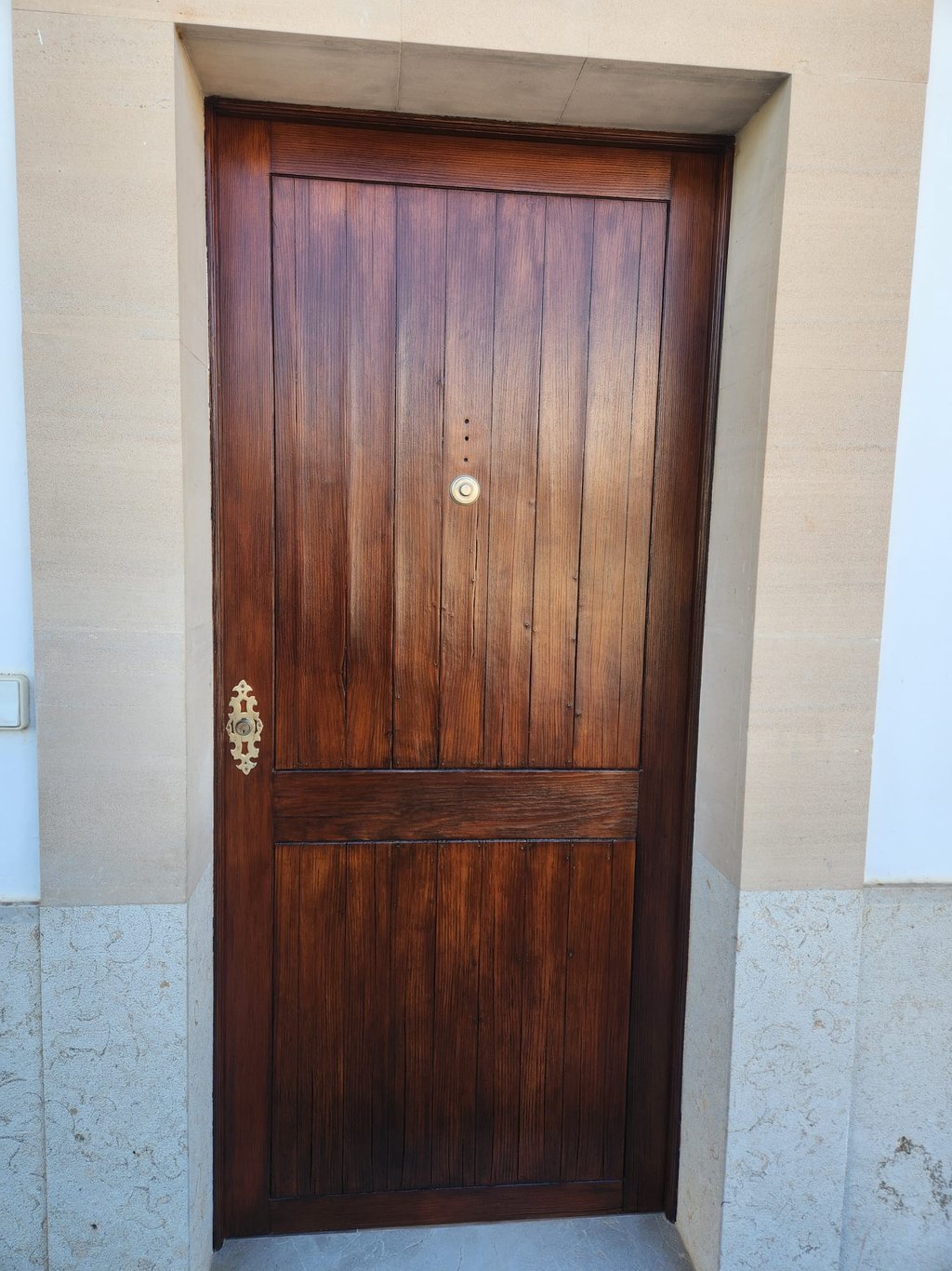 Rustic dark wood front door with vertical panels and brass hardware set in a stone archway.