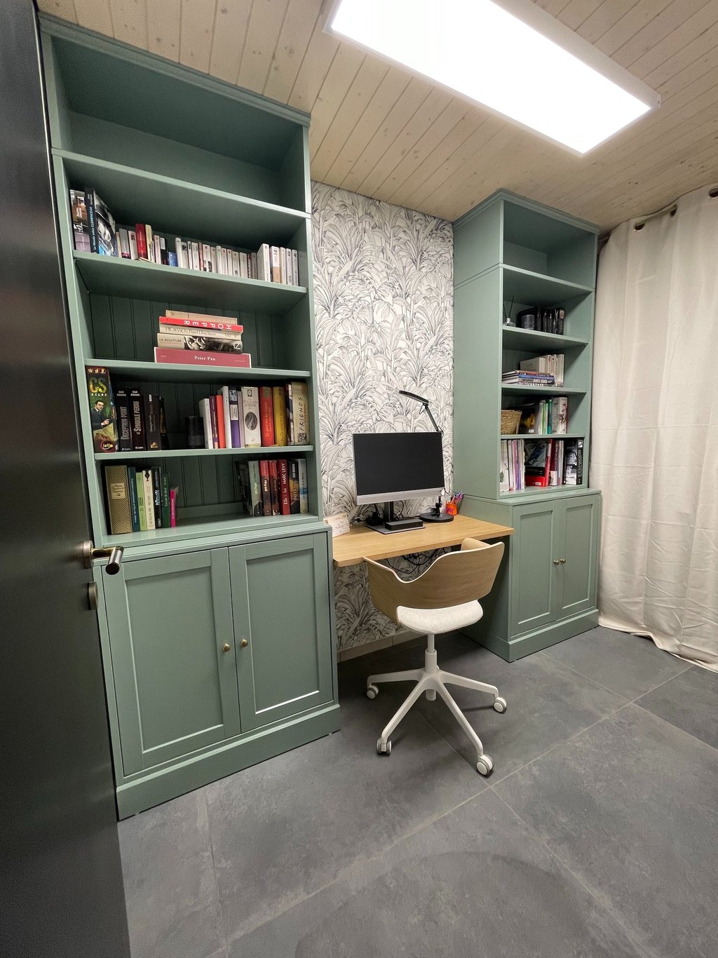 Home office with sage green built-in bookshelves, a wooden desk, and floral wallpaper.