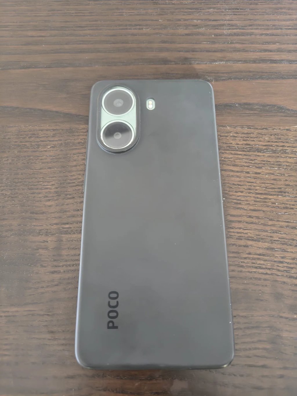 Review do telemóvel Poco mostrando o painel traseiro cinzento com lentes fotográficas sobre a mesa.