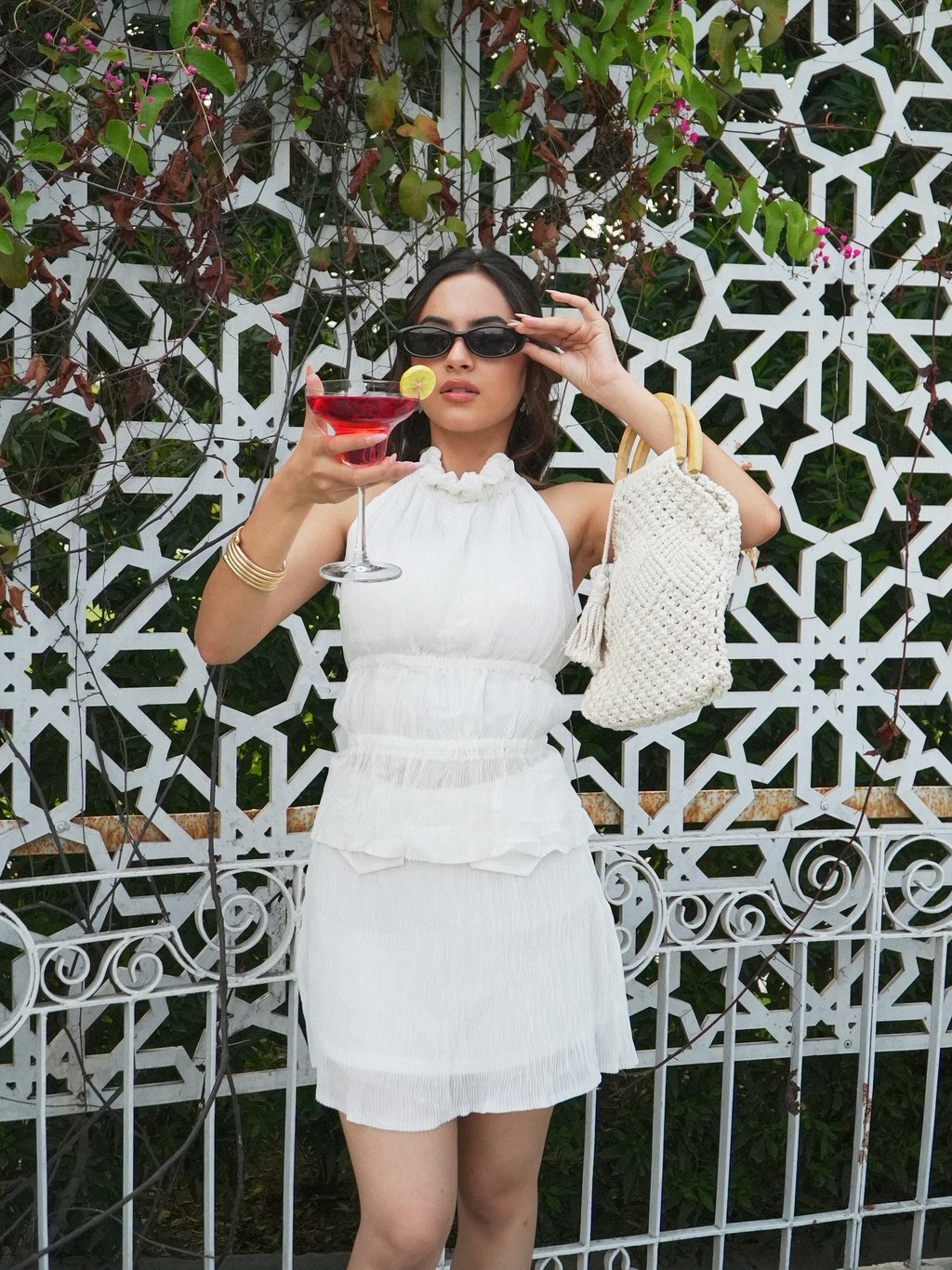 Woman in white summer dress holding a red cocktail and a woven handbag.