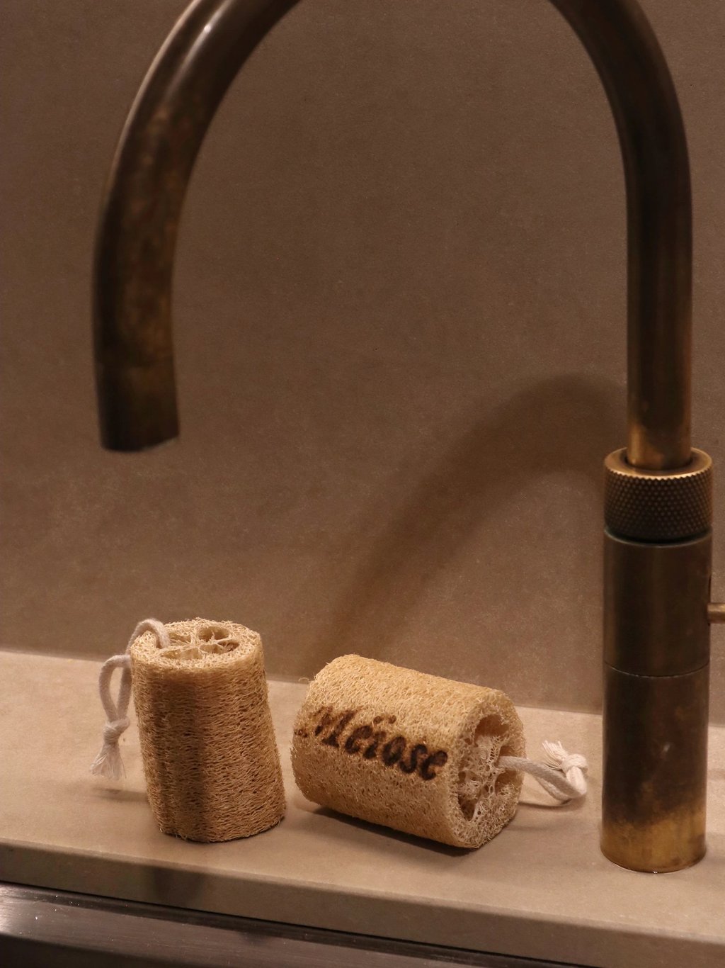 Eco-friendly natural loofah sponges with cotton loops beside a vintage brass kitchen faucet.