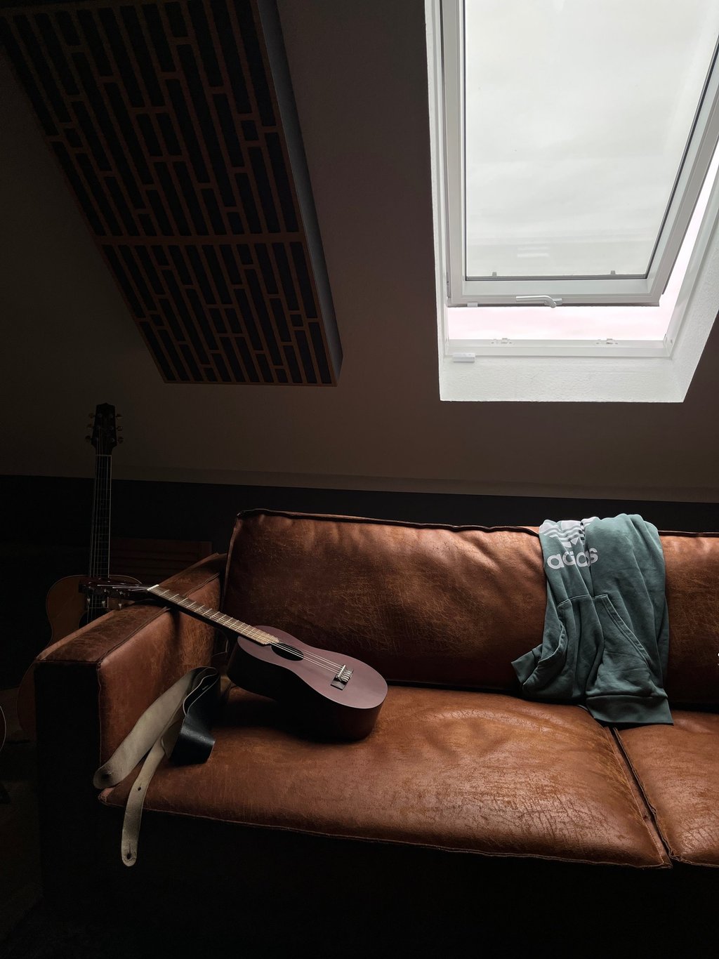 Guitar resting on leather couch under roof window in studio room