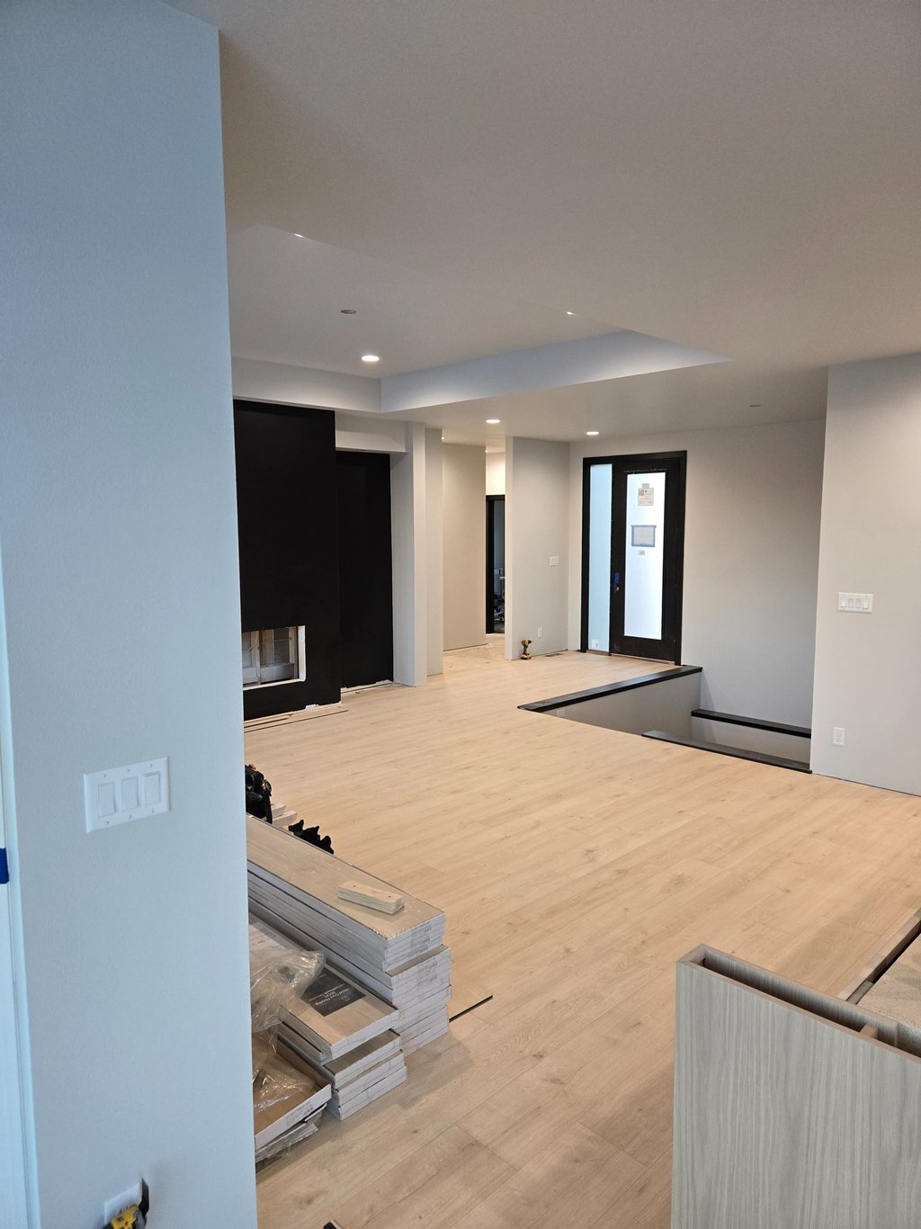 Modern home interior renovation featuring light oak luxury vinyl plank flooring and black fireplace wall.