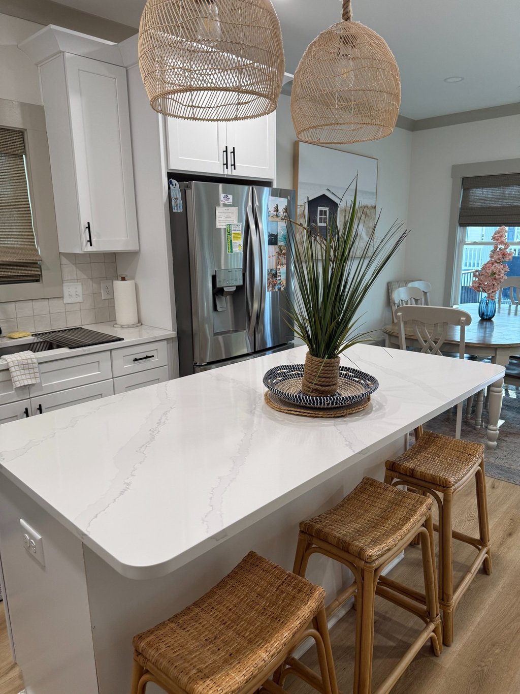 Modern white kitchen featuring a quartz island with wicker bar stools and rattan pendant lights.