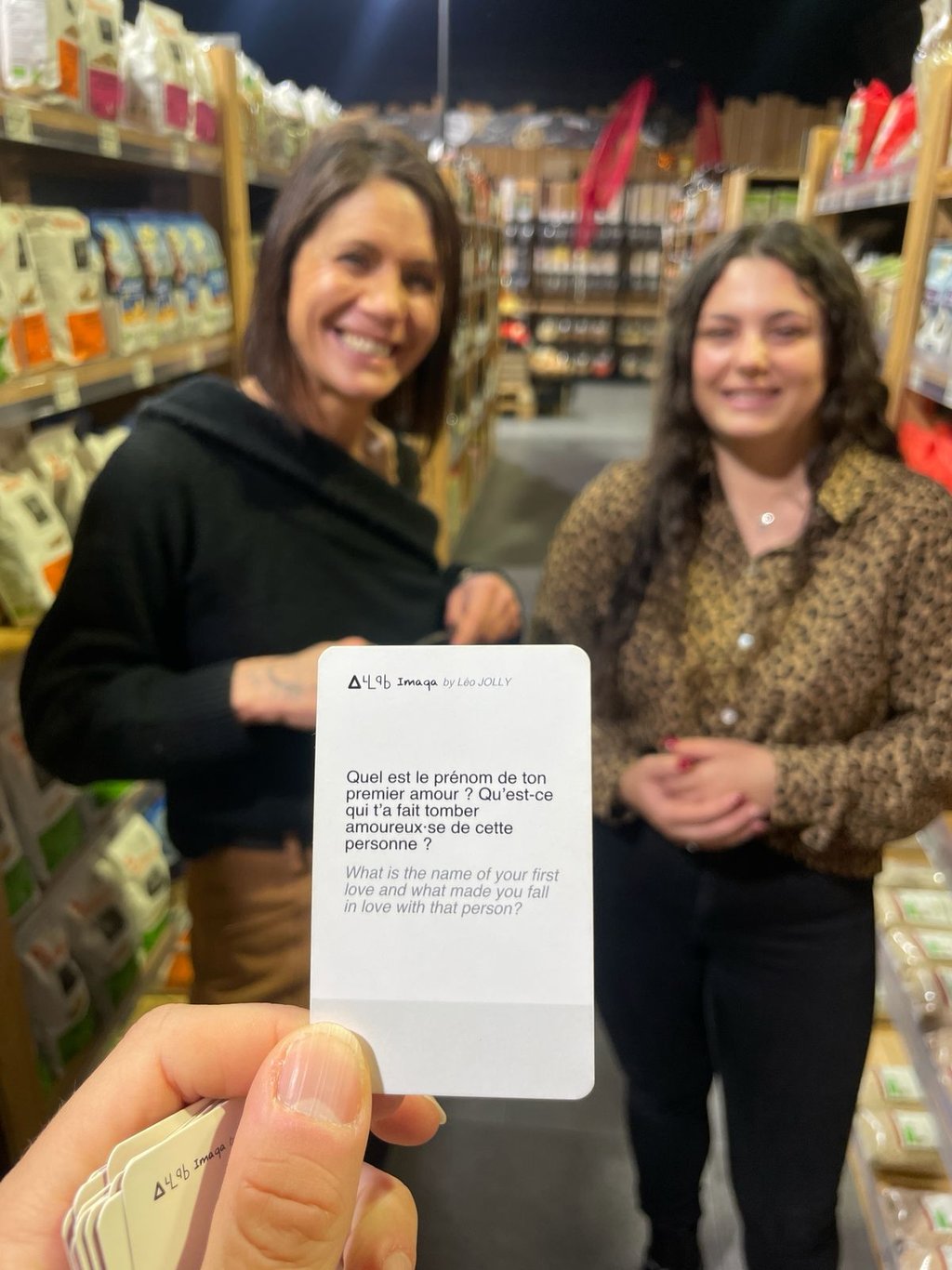 Deux femmes sourient dans un magasin derrière une fiche de conversation posant une question profonde