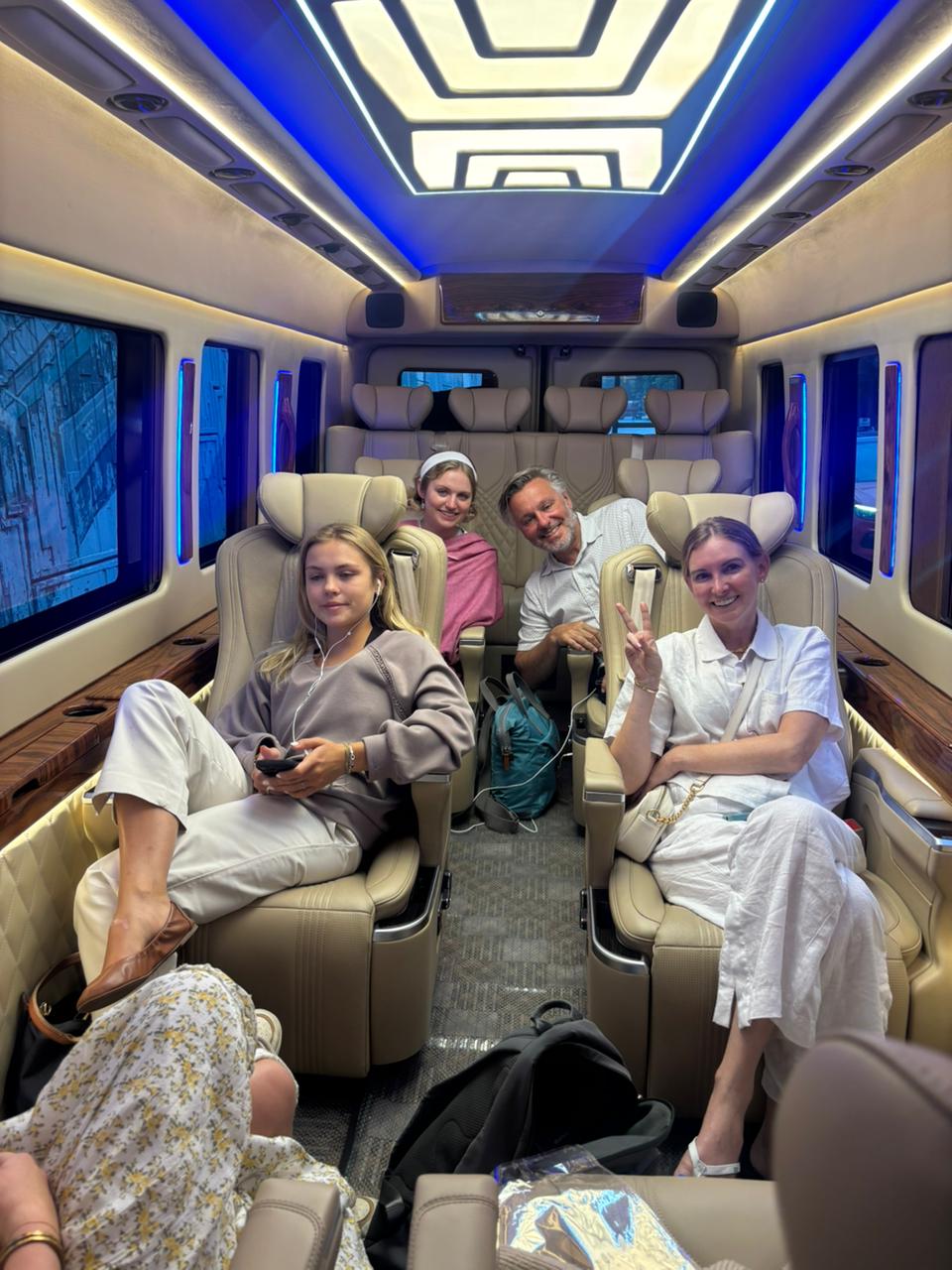 Group of four smiling passengers enjoying a premium luxury van on rent interior with blue LED lights