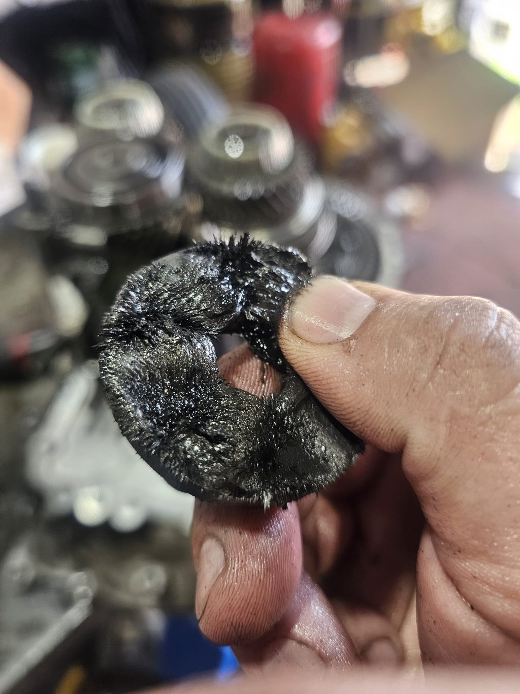 A mechanic holding a magnet covered in sharp metal shavings from a damaged car transmission.