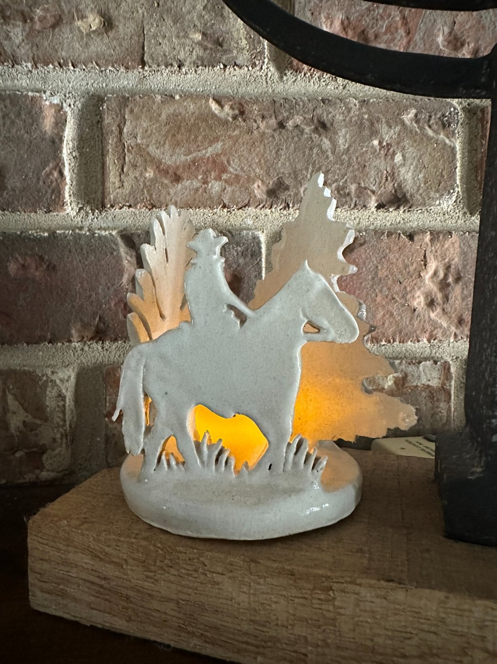 White ceramic cowboy on horse figurine with a glowing interior light set against a brick wall.