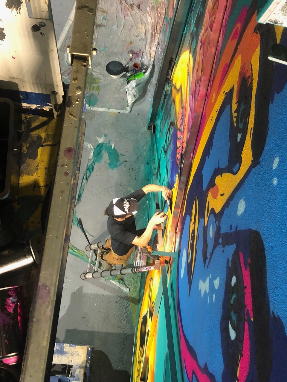 un homme vu de haut entrain de peindre une fresque sur une échelle 