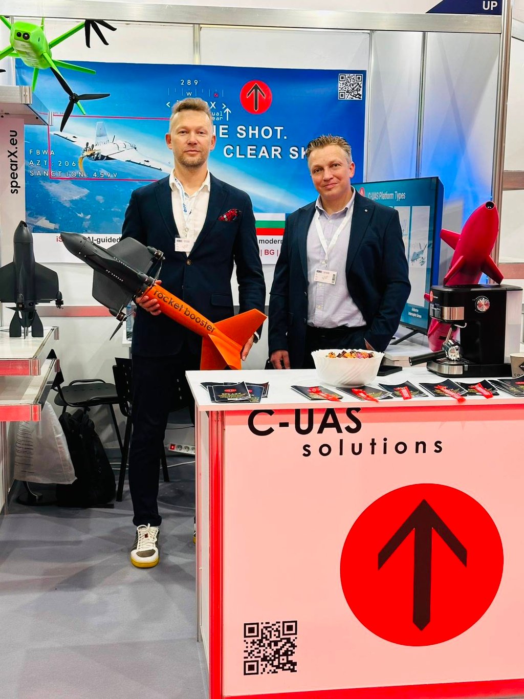 presenting high-tech C-UAS drone defense solutions and a rocket booster at a technology trade show booth.