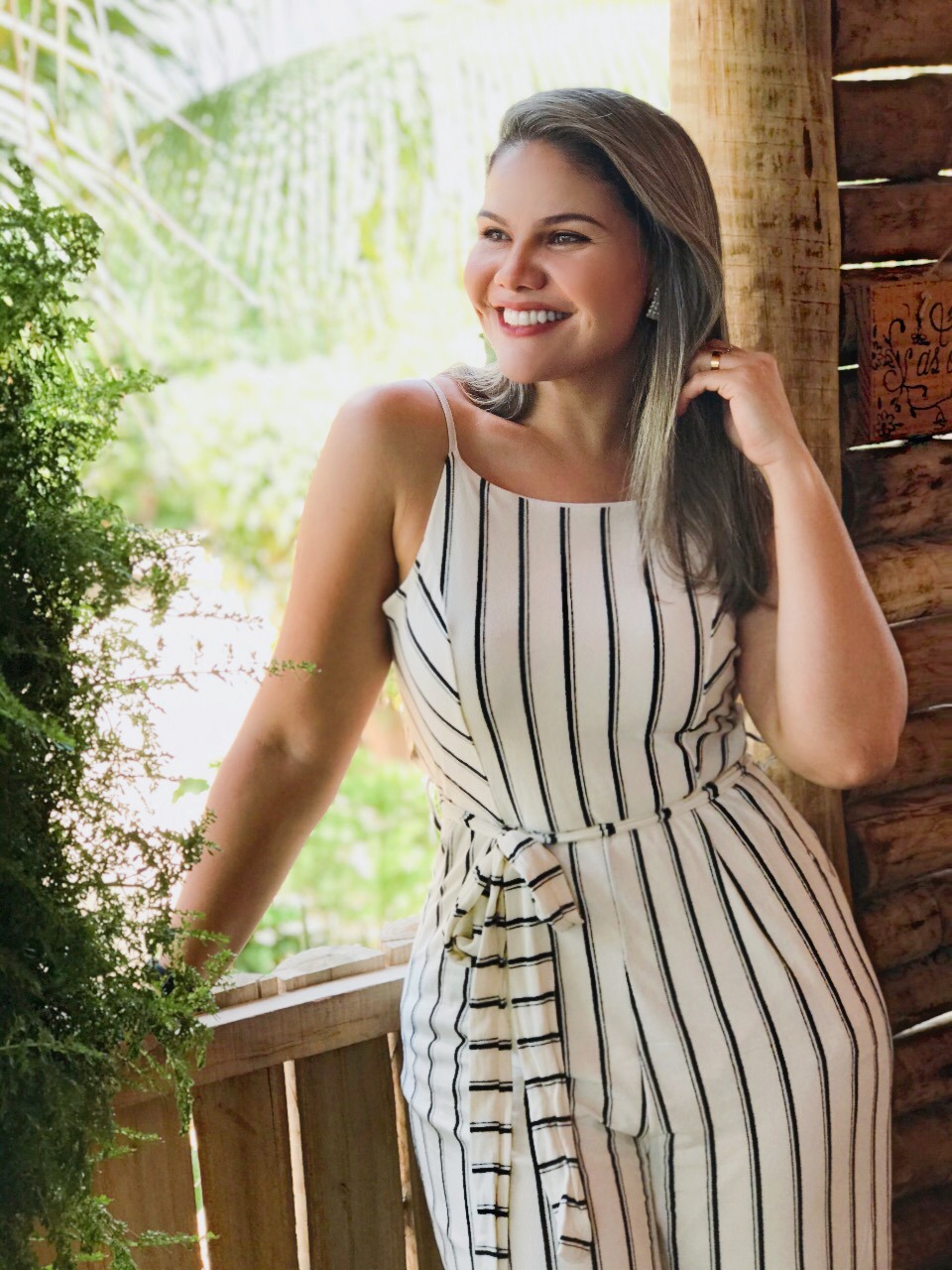 Priscila, Pri Cílios extensionista de cílios, sorrindo em fazenda com vestido branco.
