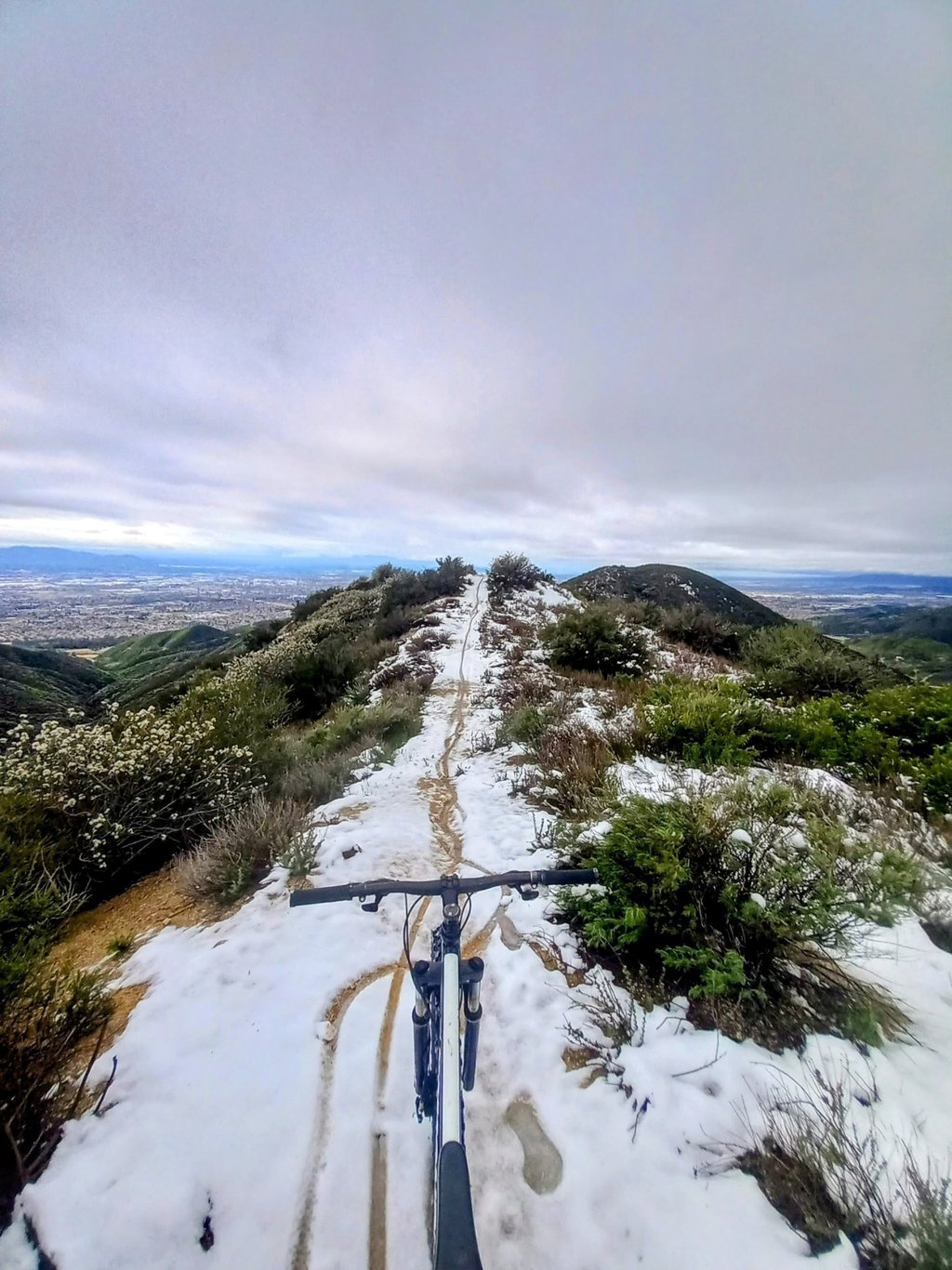 Mountain bike POV riding snowy trail in Southern California with city views below