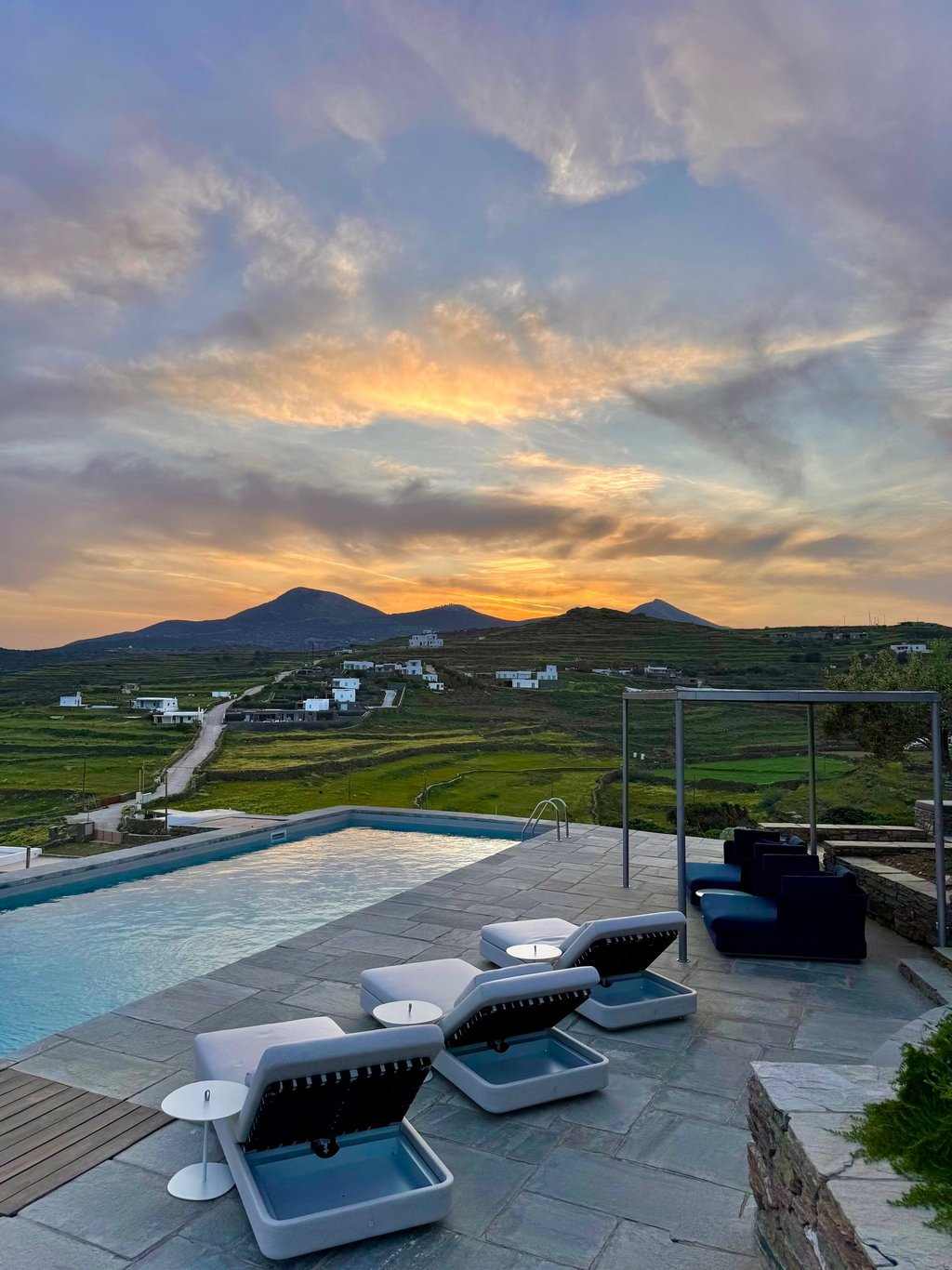 View over the pool onto green hills and small buildings in the distance.
