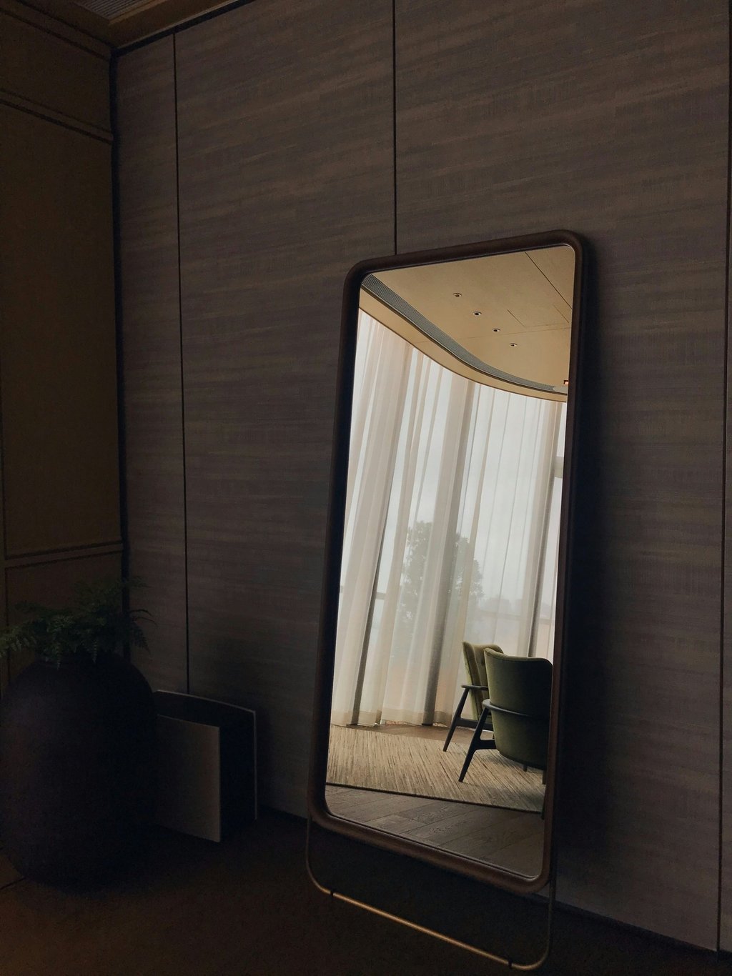 Full-length floor mirror against dark wood panel wall in luxury interior