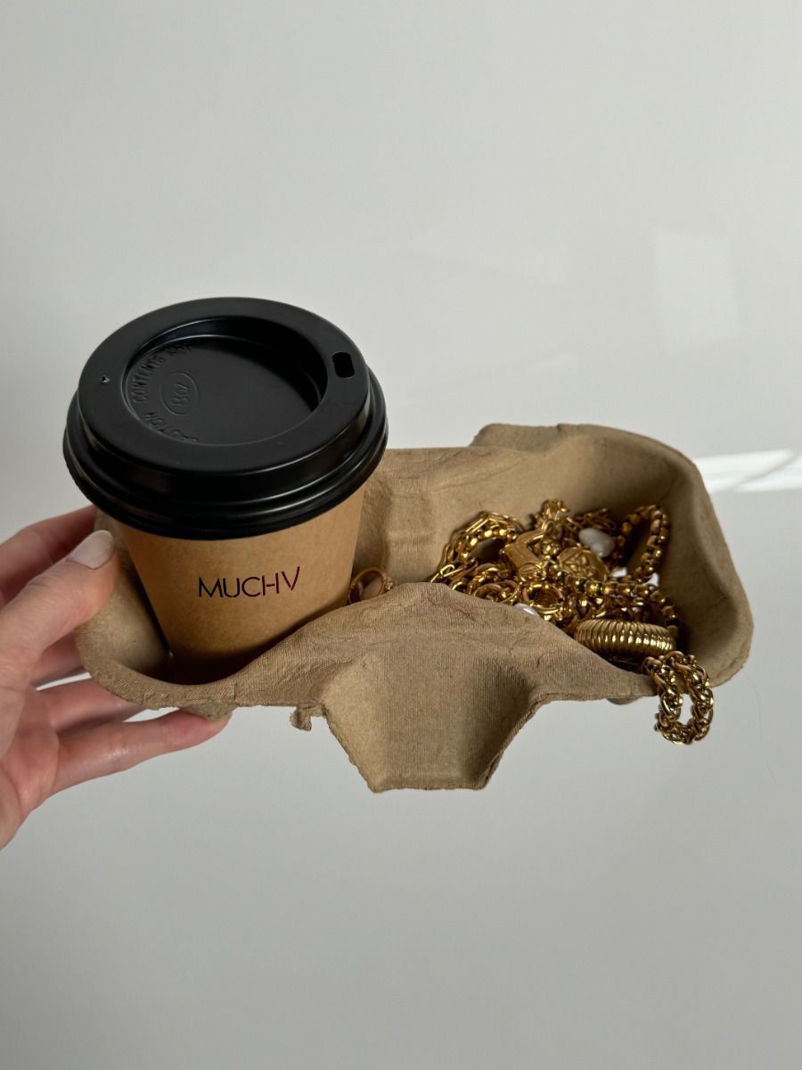 Hand holding a cardboard cup carrier with a takeaway coffee and gold chunky chain jewelry.