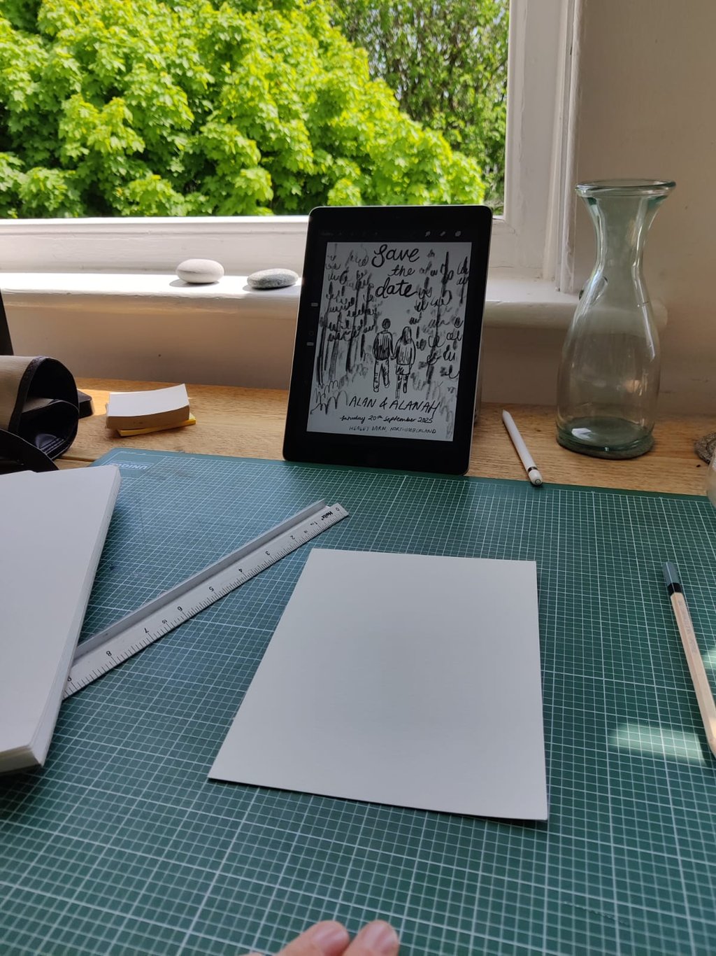 Eleanor's (elsillustrations) hand holding a pen and a tablet with a  sketch of the save the dates