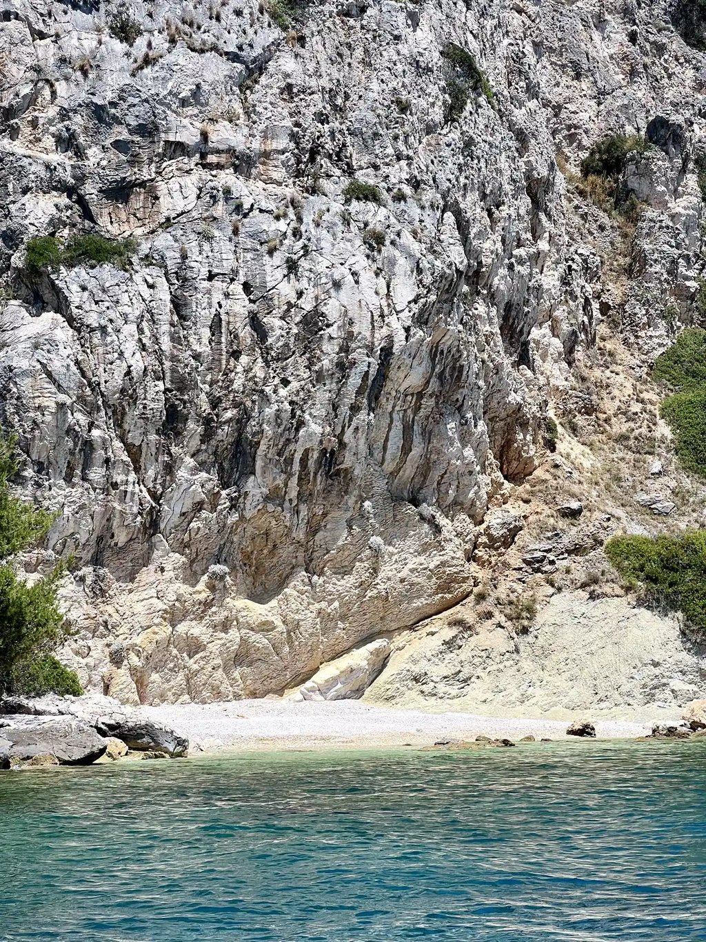 Sea level view of the hidden beach under cliffs on Ciovo Island, seen on a private boat tour off the coast of Split, Croatia.