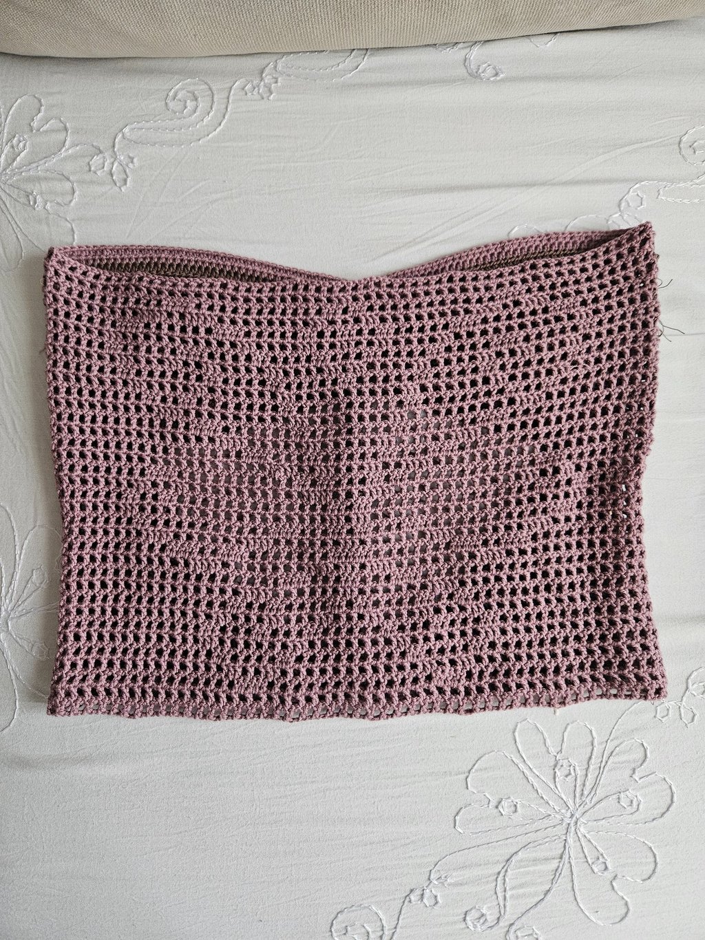 Handmade mauve crochet tube top with a mesh stitch pattern laying flat on a white floral fabric.