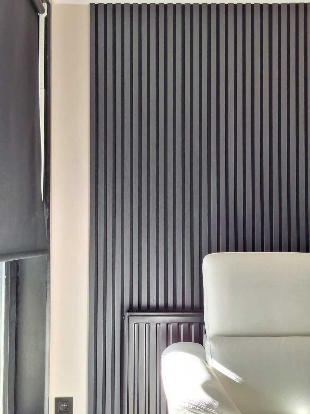 Zoom sur un radiateur peint en noir devant des lattes de bois noires et un bout de canapé blanc
