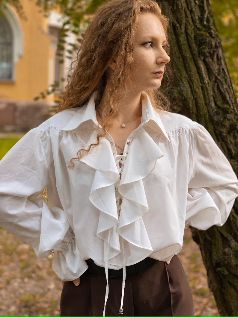 A woman with red-blonde hair wearing a white poet shirt, with a large collar and ruffled front.