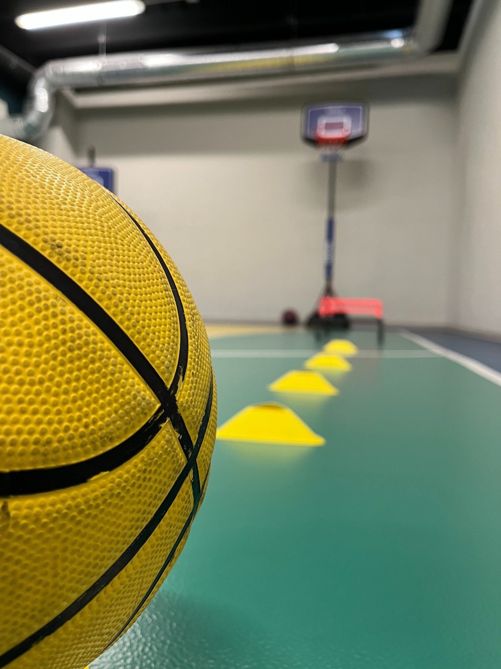 Primo piano di un pallone da basket giallo in un'area multisport della palestra Move 2 Grow a Milano, con coni e canestro sul