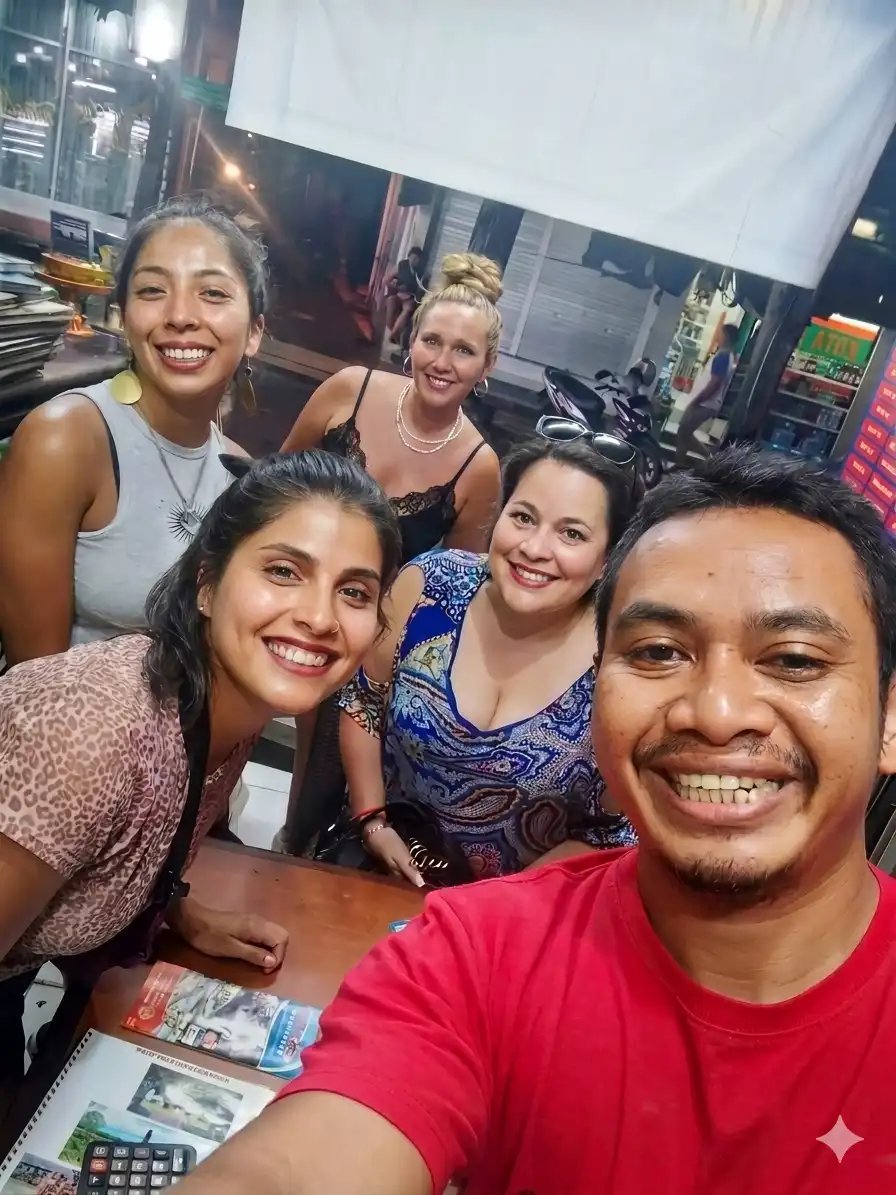 A group of happy diverse friends smiling for a group selfie while dining at an outdoor night market restaurant.