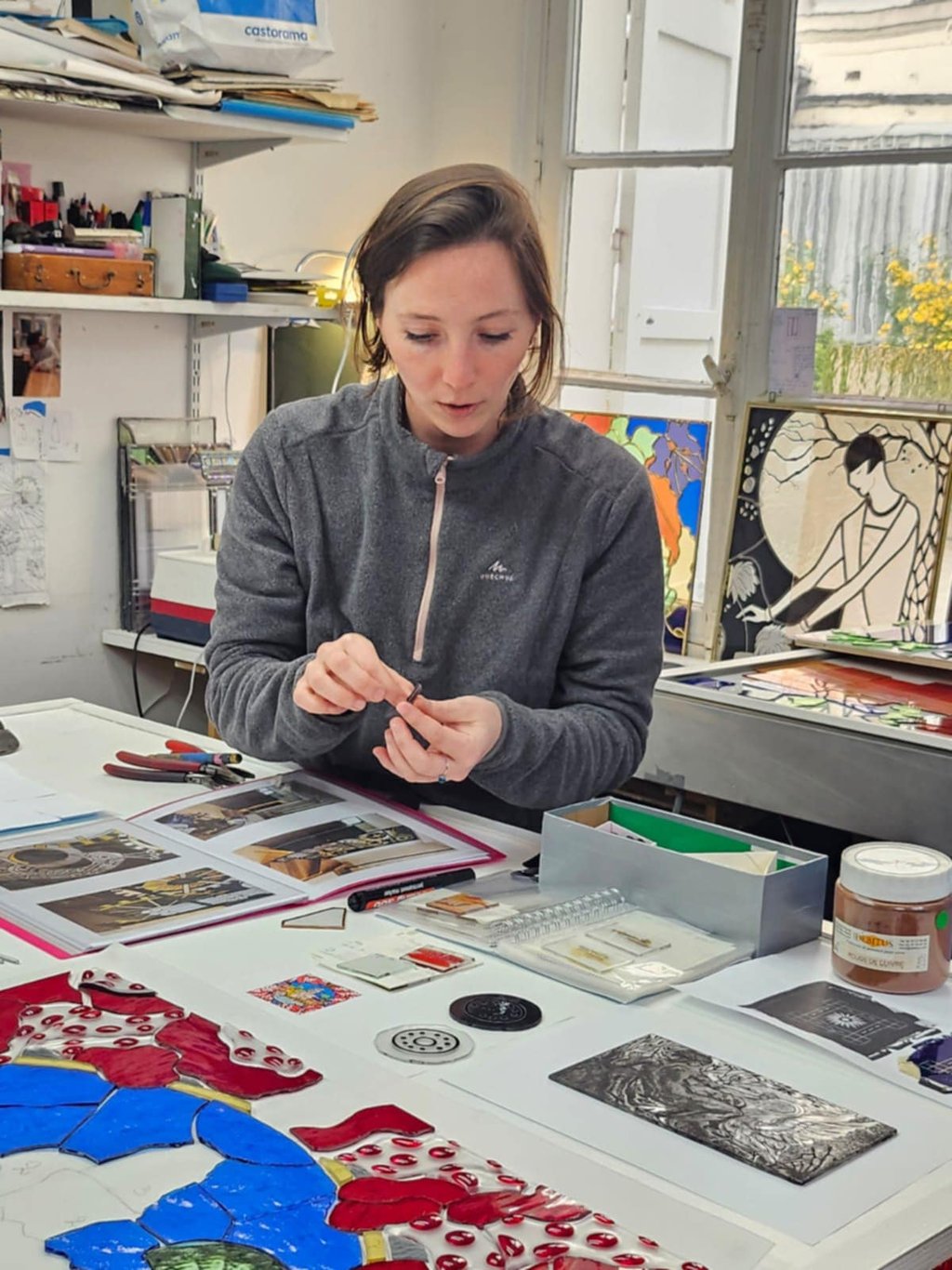 Geste artisanal d'Édith Théret assemblant avec précision des pièces de verre pour un vitrail.