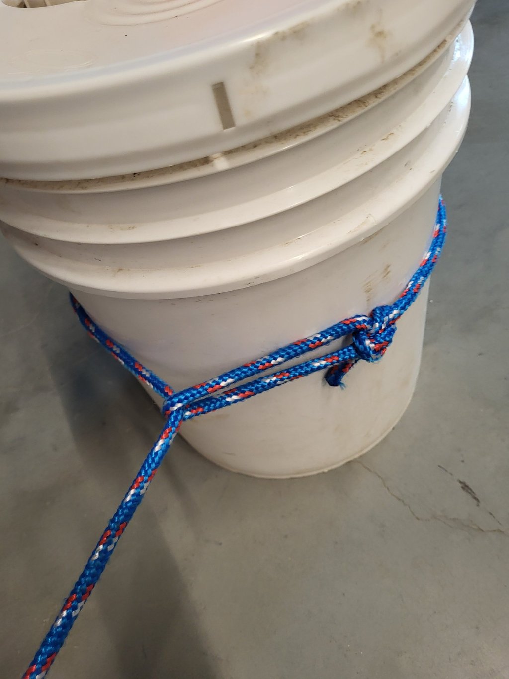 Close up of a running bowline knot tied with blue synthetic rope around a bucket.