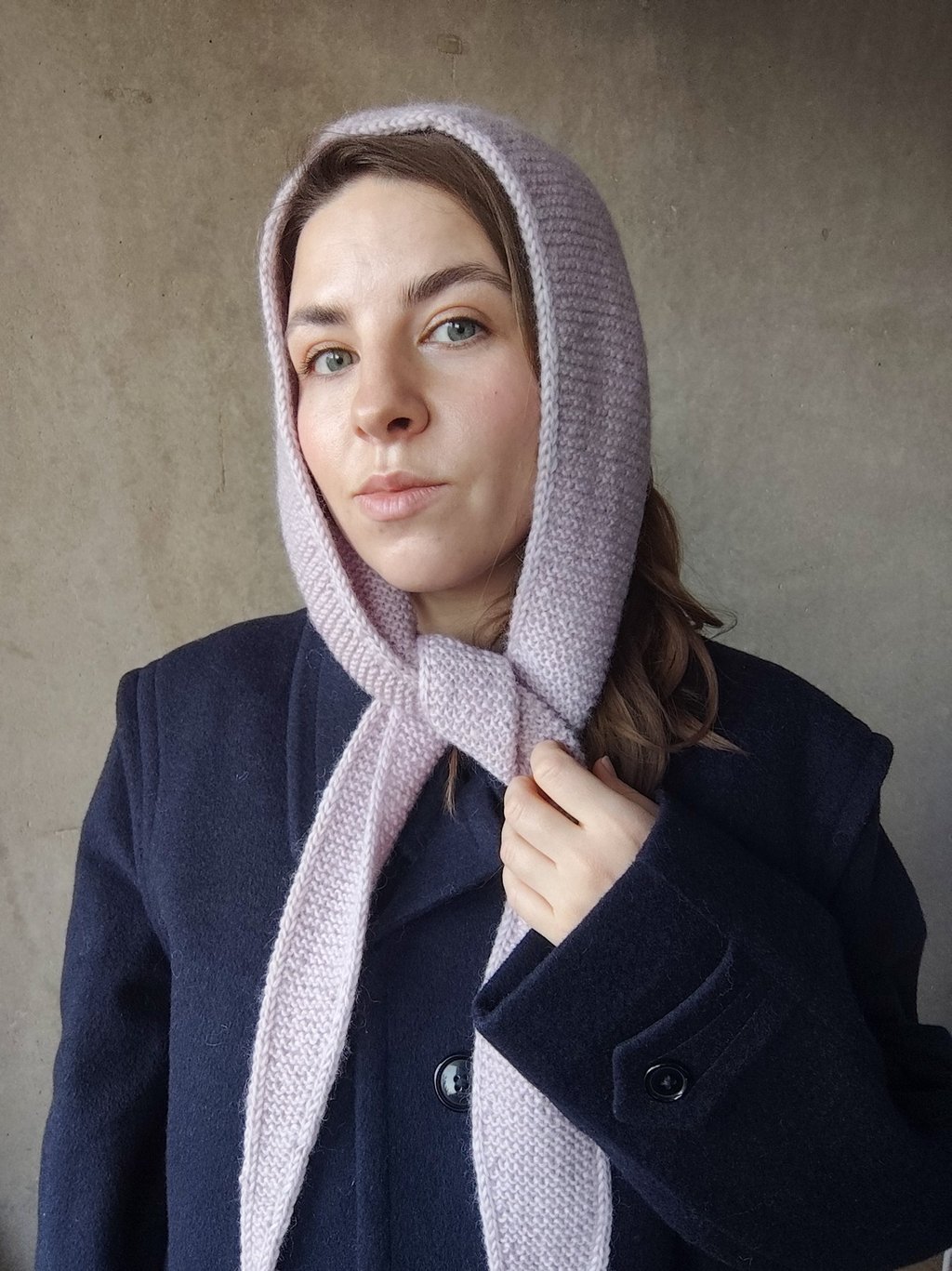 kobieta z wełnianym szalem na głowie na tle szarej ściany