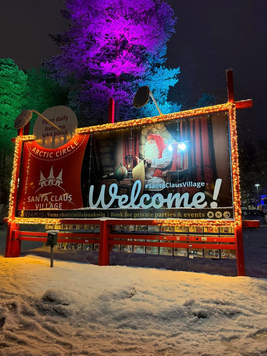 Illuminated Santa Claus Village welcome sign at the Arctic Circle in Rovaniemi Finland at night.
