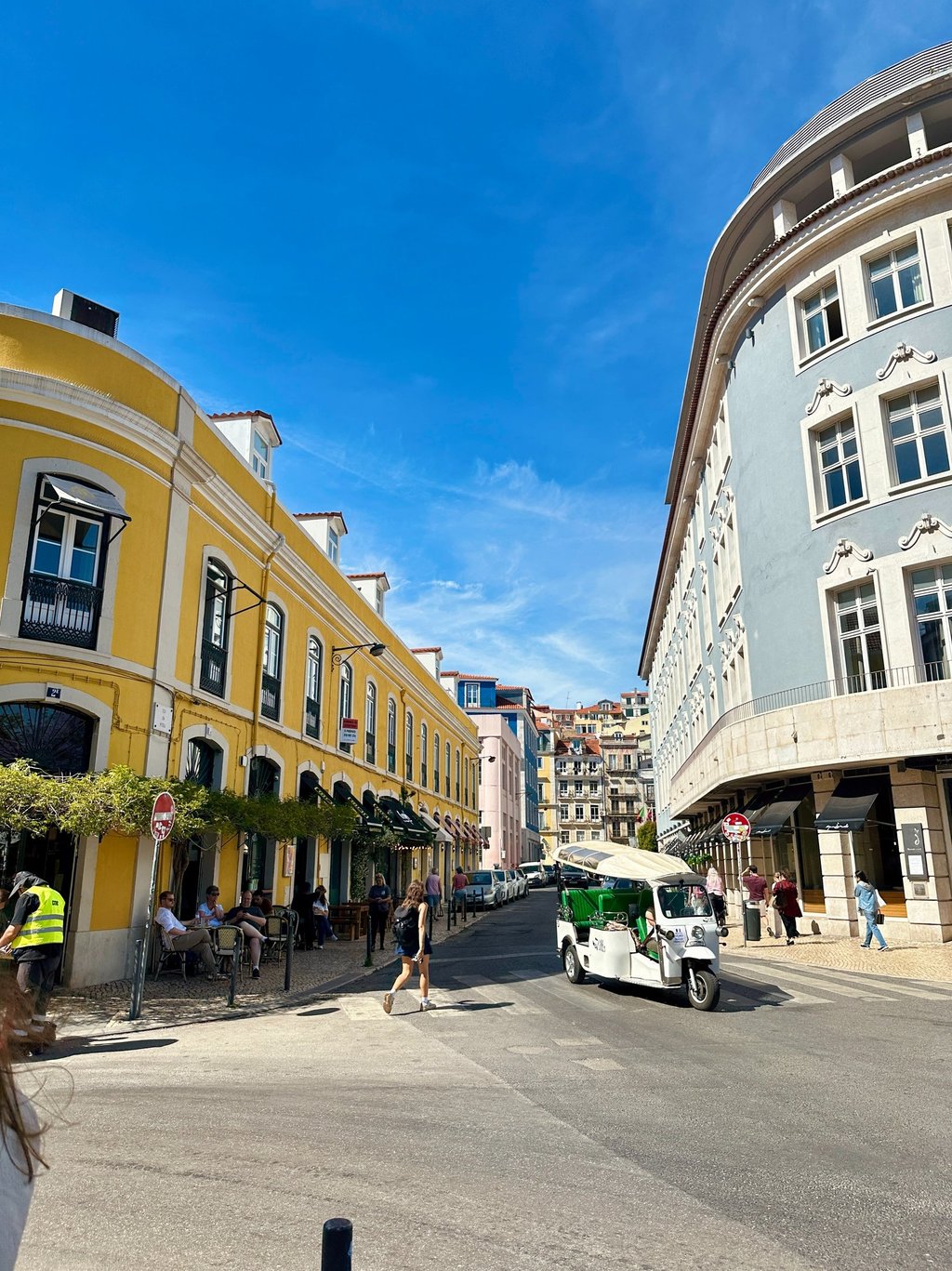 Prédios, um estrada, pessoas em bares e um tuk tuk