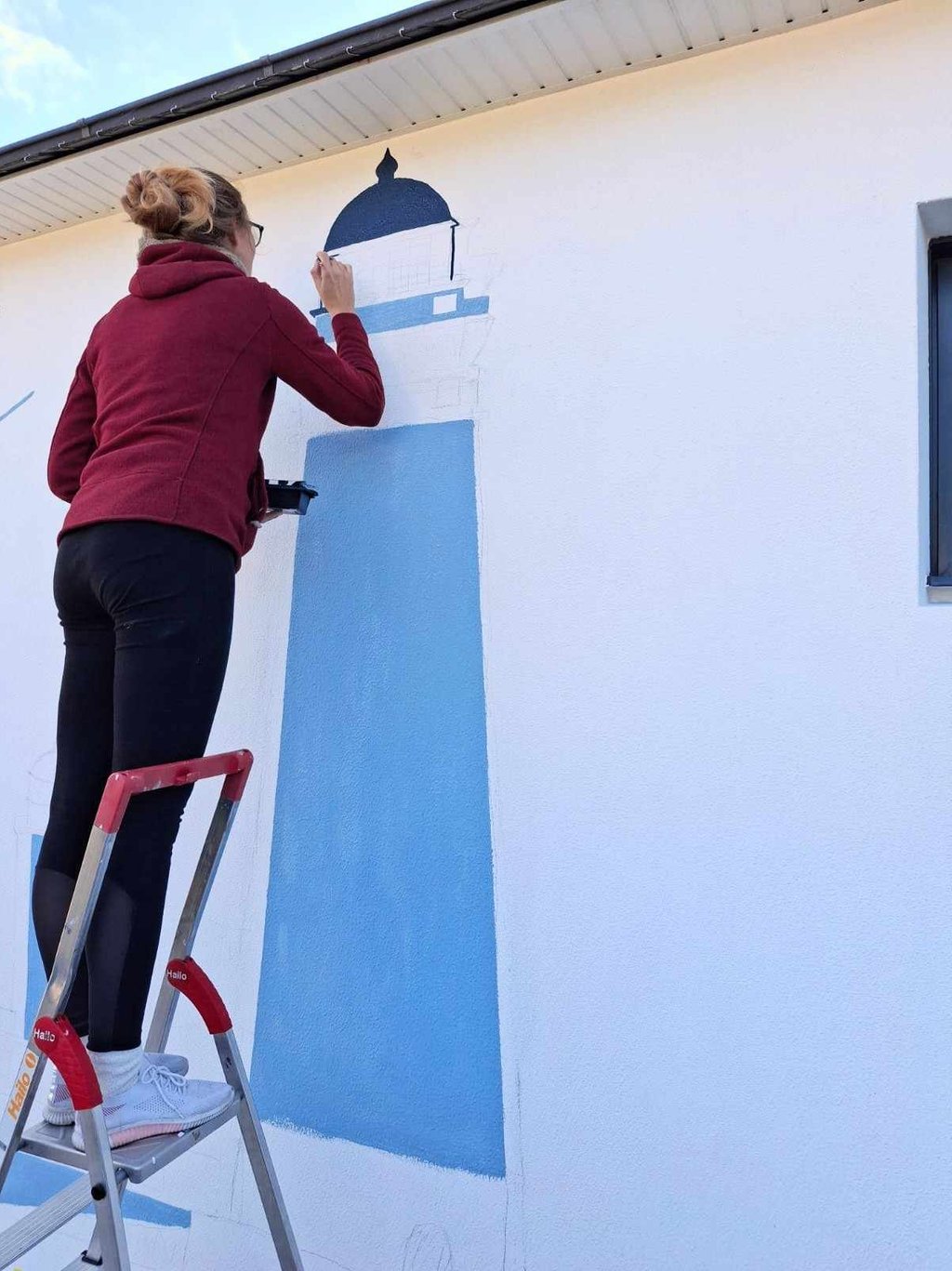 Artiste en train de peindre une fresque bleue sur un mur de maison