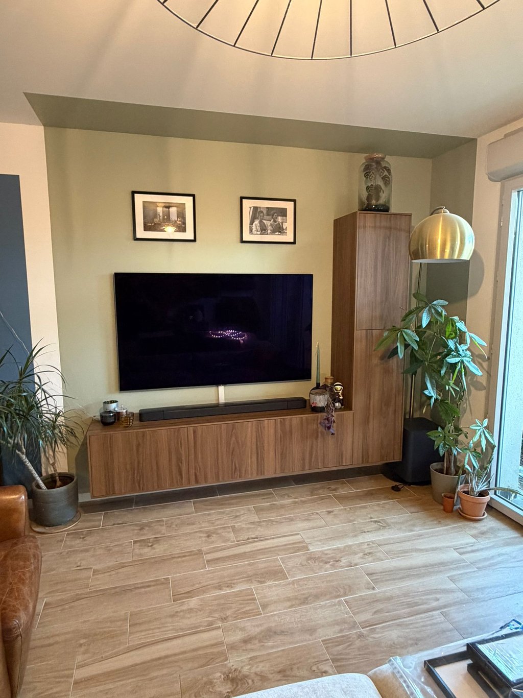 Rénovation salon à La Ciotat : grand meuble TV suspendu en bois, mur vert olive et plantes vertes.