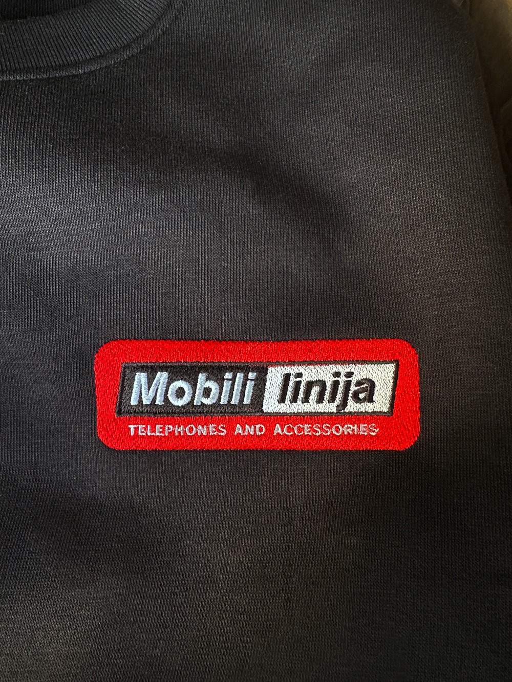 Embroidered Mobili linija logo on a black sweatshirt for telephones and accessories branding. 