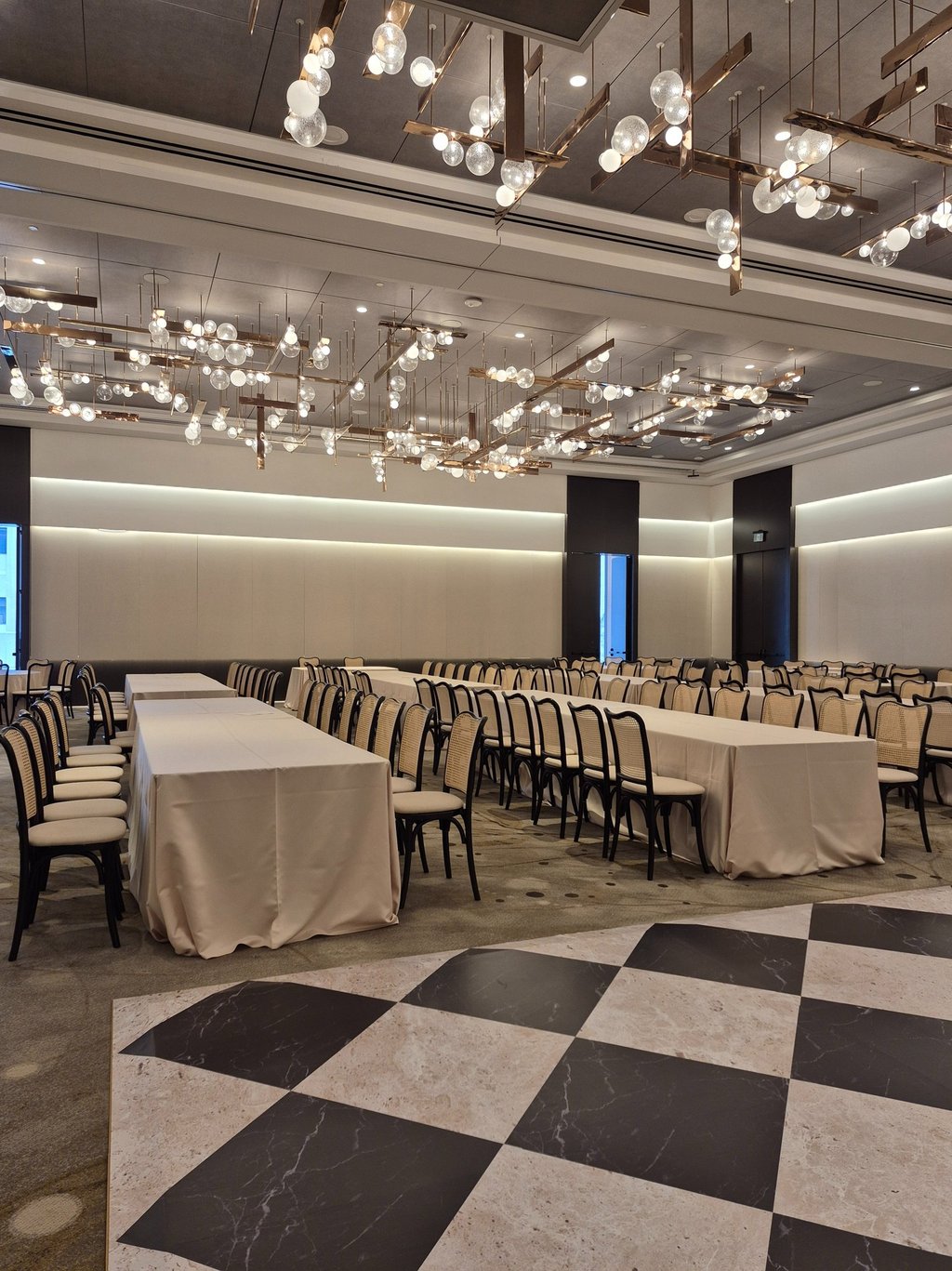Modern banquet hall setup with long tables, neutral décor, and contemporary chandelier lighting