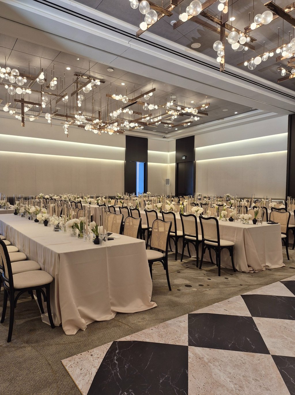 Elegant banquet hall setup with long tables, white floral arrangements, and modern chandelier