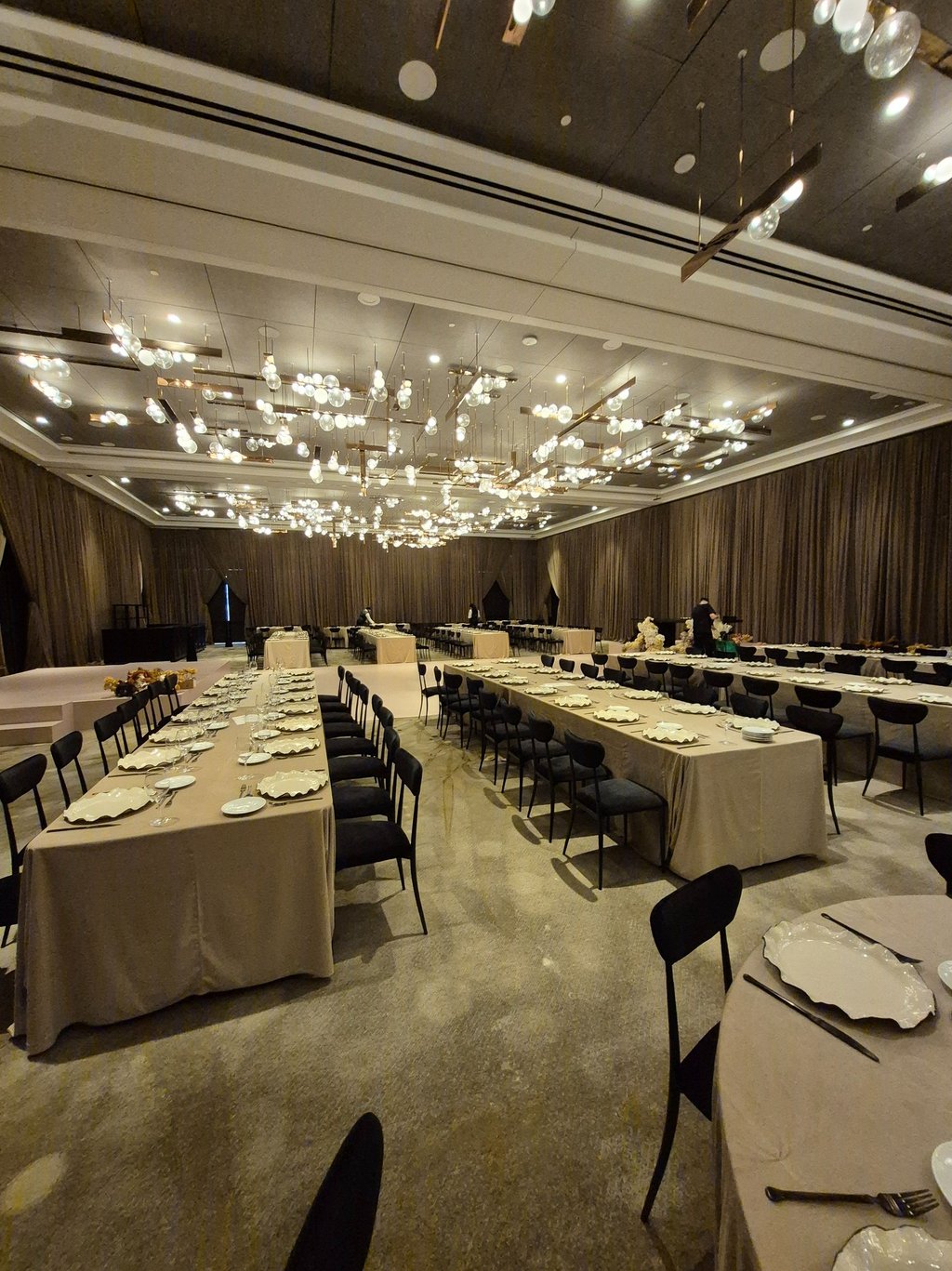 Luxury event setup featuring long dining tables, neutral linens and black seating