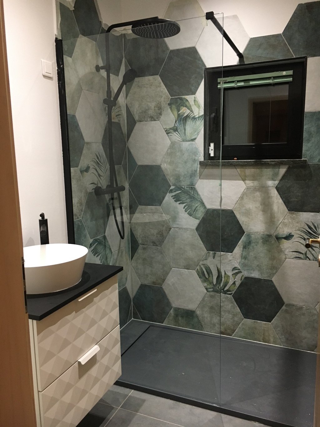 Modern bathroom featuring green floral hexagonal wall tiles and a matte black walk-in rain shower.