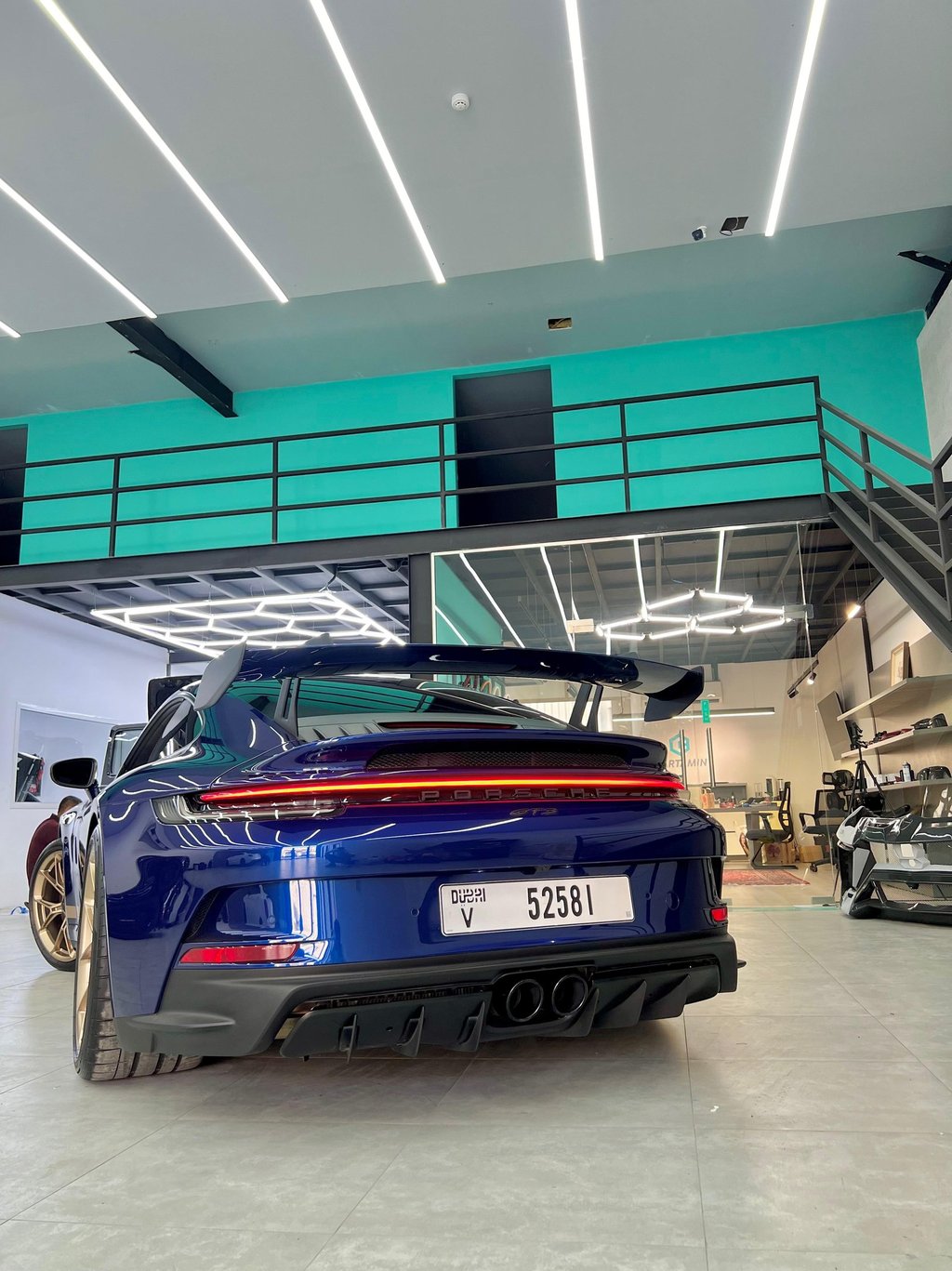 Rear view of a blue Porsche 911 GT3 with a large spoiler in a modern automotive detailing garage.