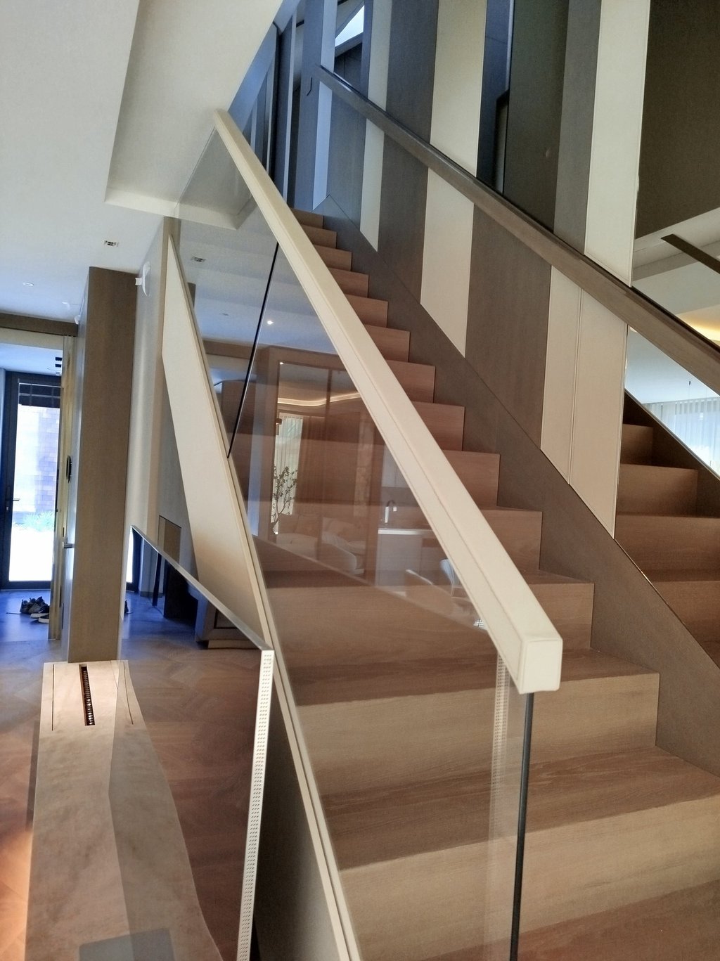 Modern interior staircase featuring light wood steps and a minimalist glass railing with white handrails.