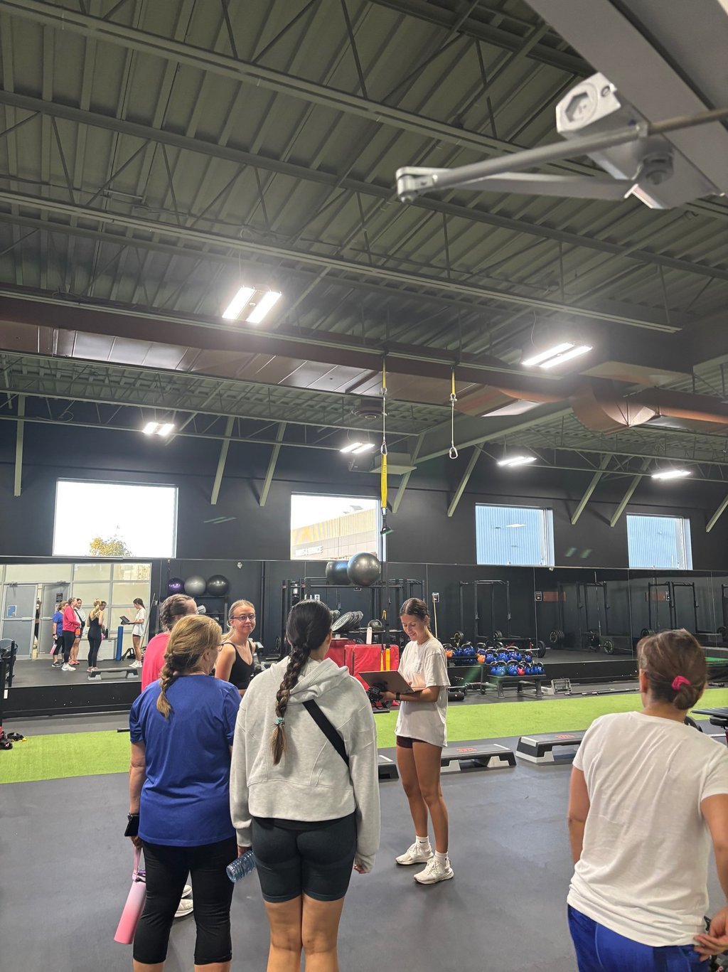 A group of women in a fitness center receive instruction from a trainer during a group workout session.