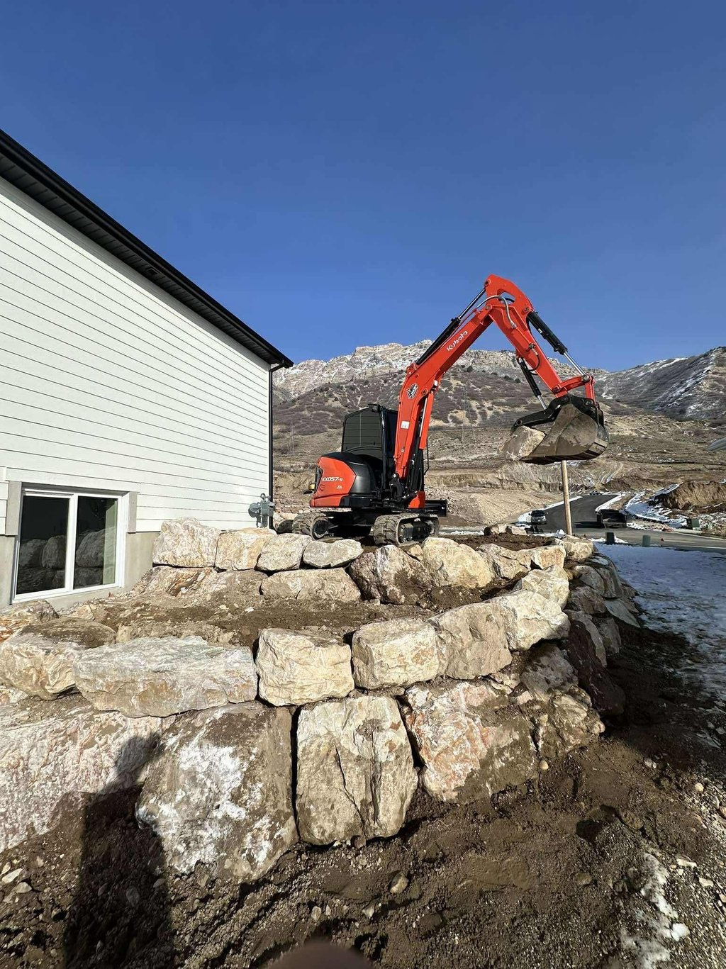 Kubota mini excavator hauling a rock as a boulder wall is being built