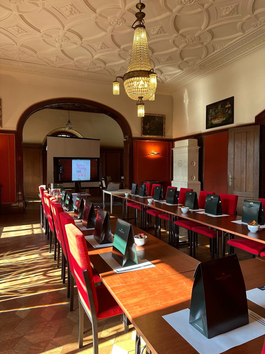 Elegant conference room with red chairs, wooden tables, and a crystal chandelier for corporate events.