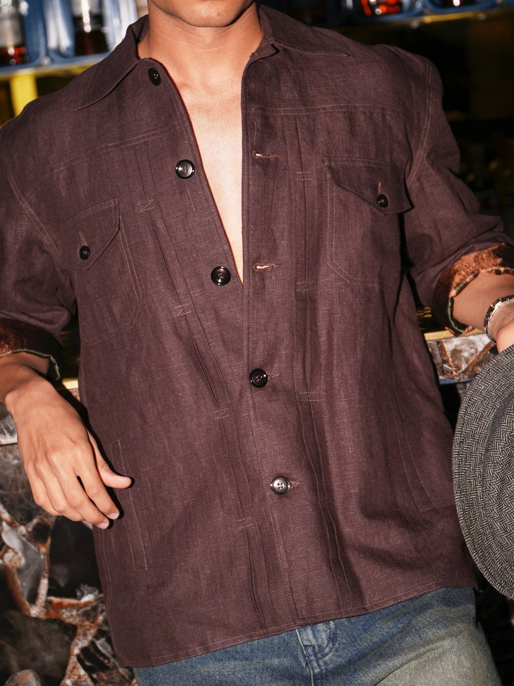 A man wearing a stylish brown linen button-down shirt with chest pockets and blue denim jeans.